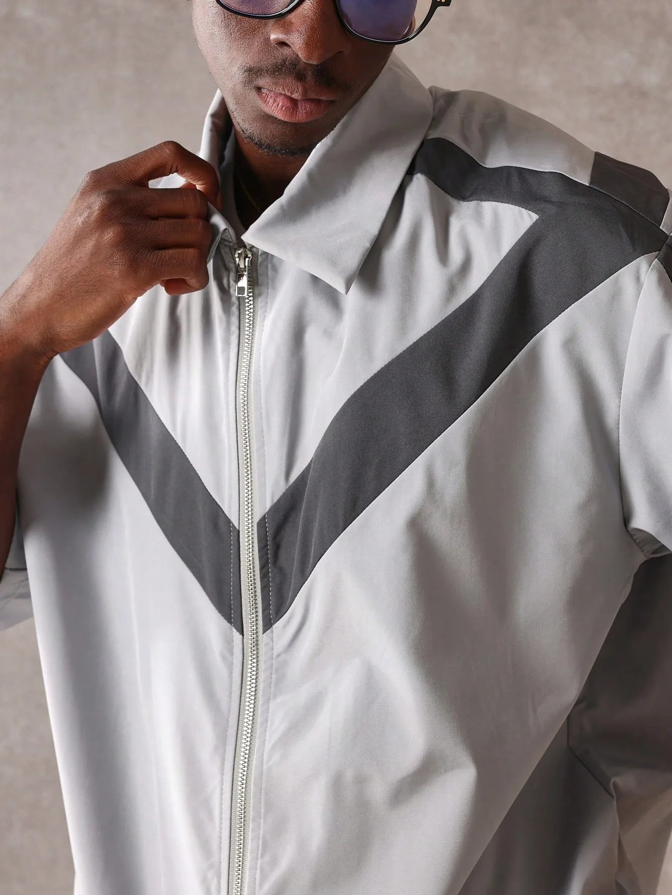 Person wearing a white jacket with grey accents and sunglasses, against a neutral background