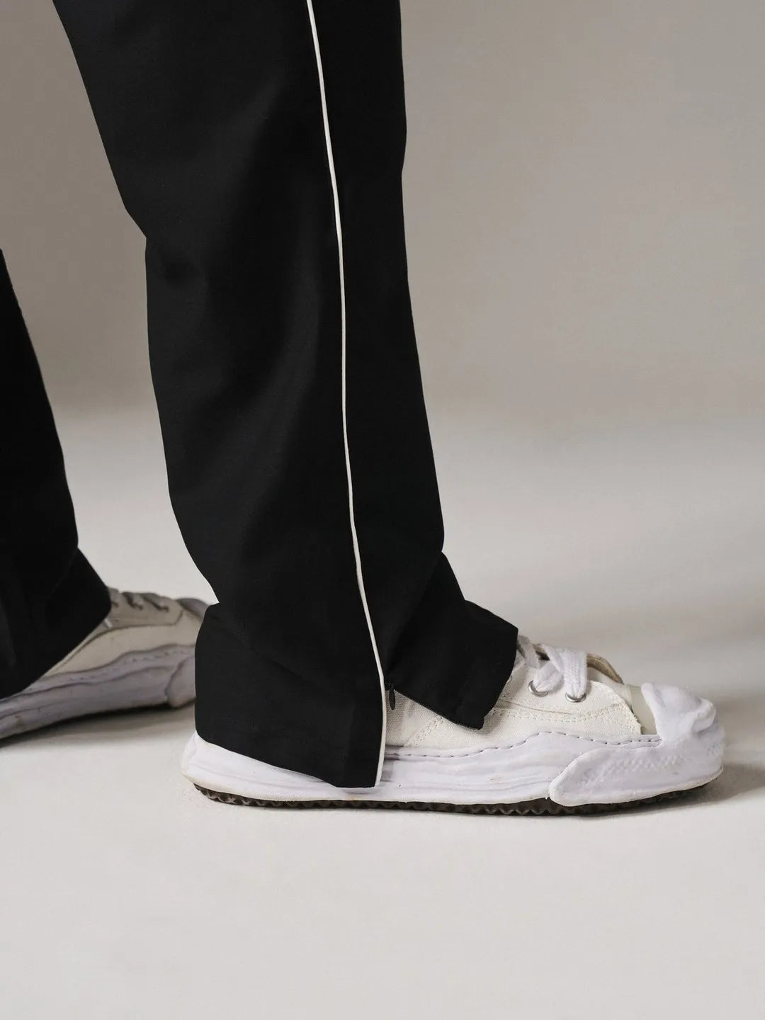 Person wearing black pants with white stripes and white sneakers on a neutral background