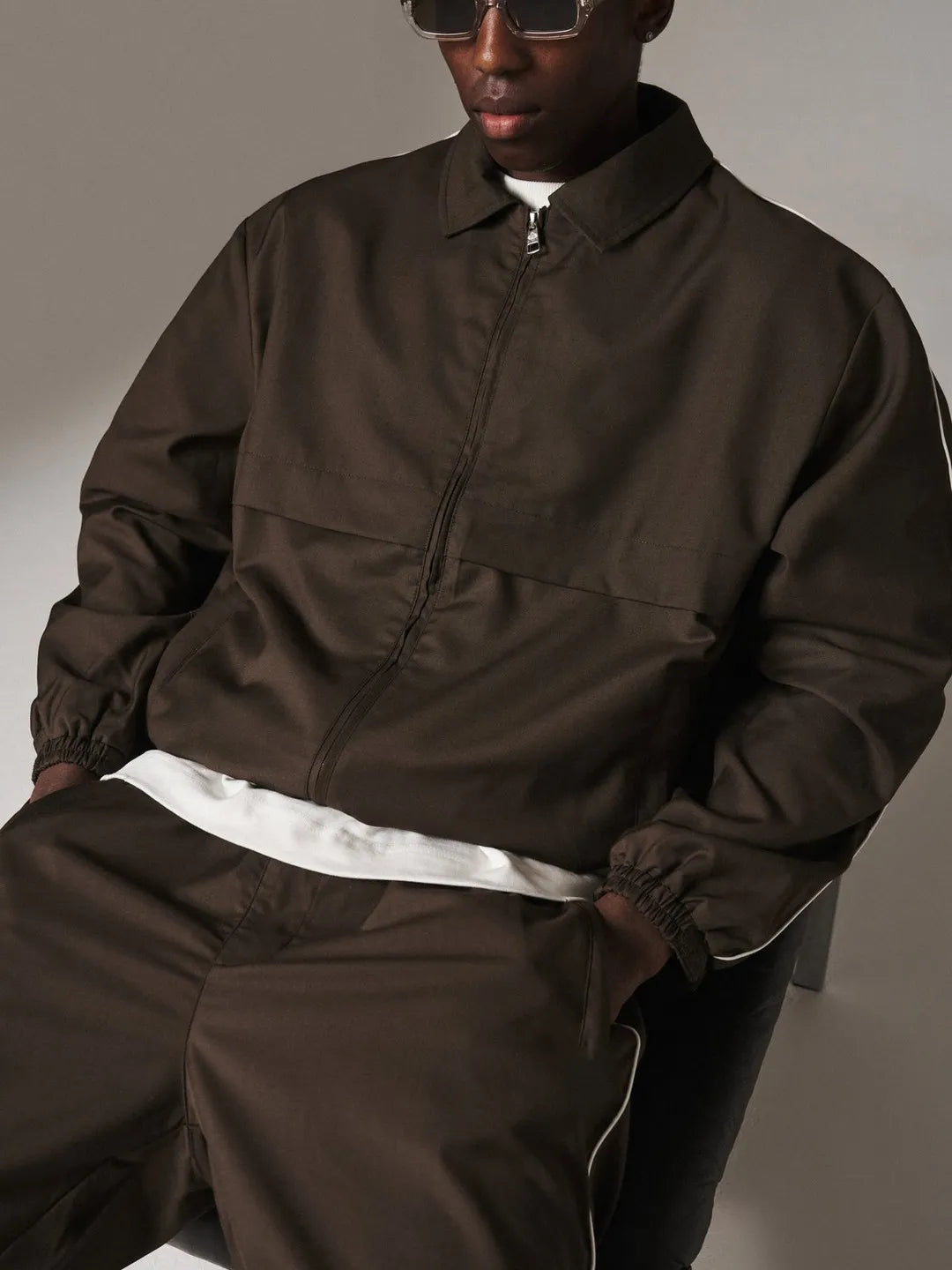 Person wearing a brown tracksuit sitting against a neutral background
