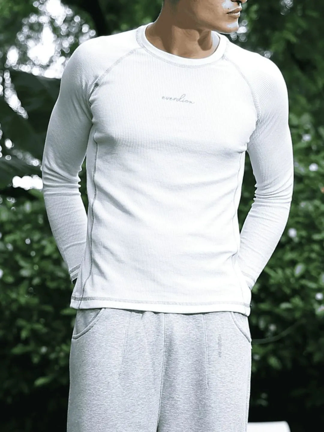 Person wearing a white long-sleeve shirt and gray pants against a blurred green background