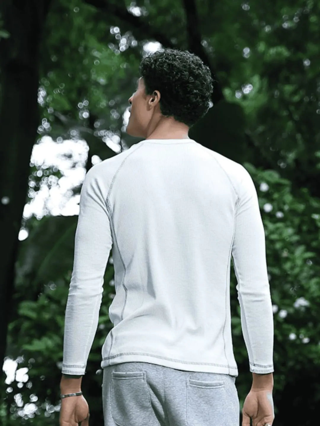 Person wearing a white long-sleeve shirt and grey pants standing in a forest