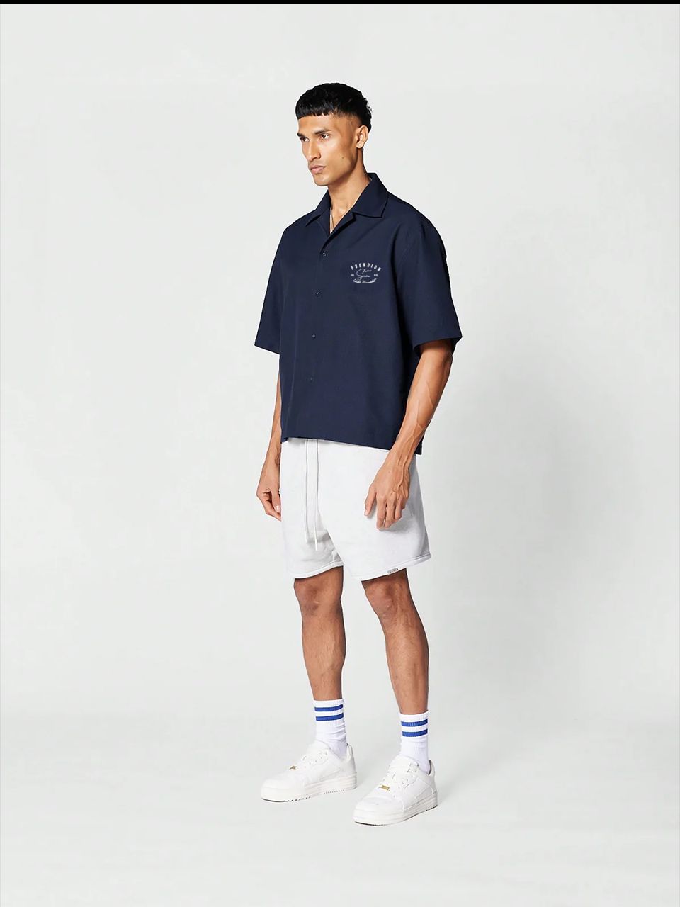 A man wearing a navy blue, oversized, half-sleeve bowling shirt with a crew neckline, featuring a small signature print on the front.