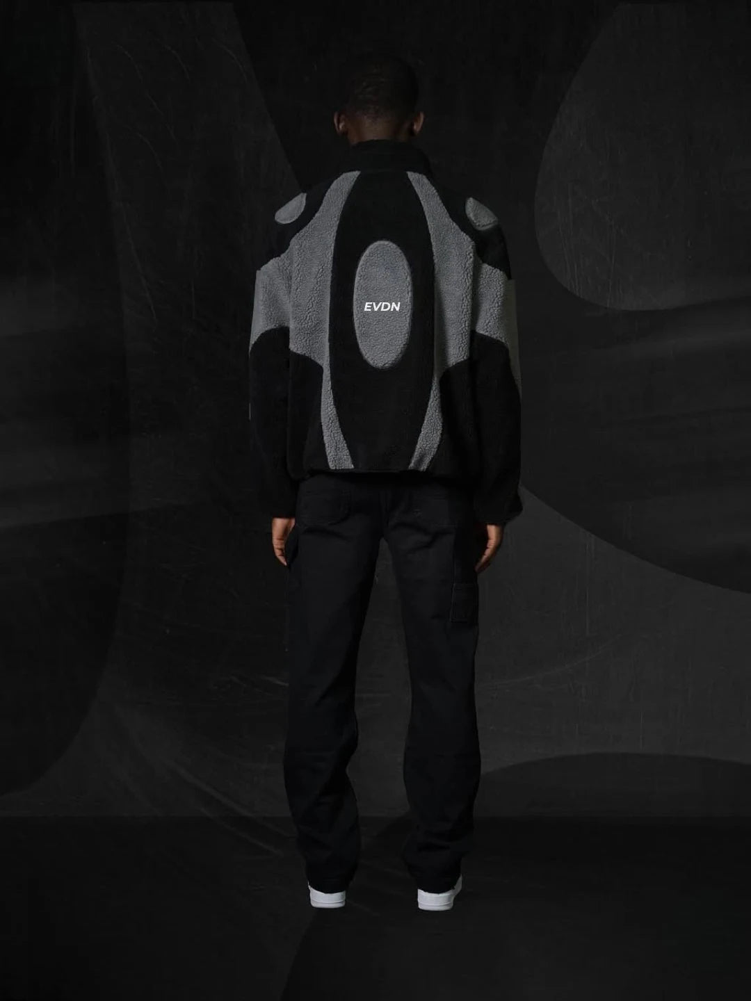 Person wearing a black and gray jacket with 'EVDN' branding on a dark background
