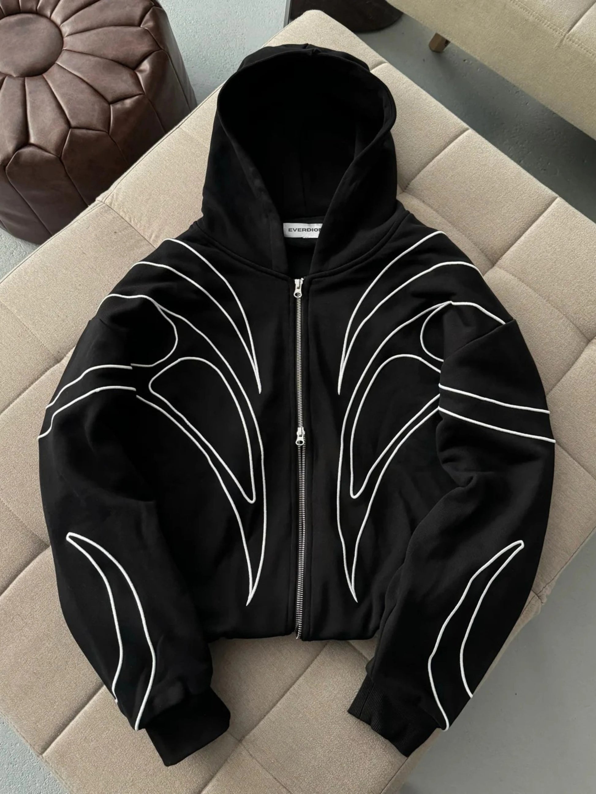 Black hoodie with white designs on a beige cushioned surface