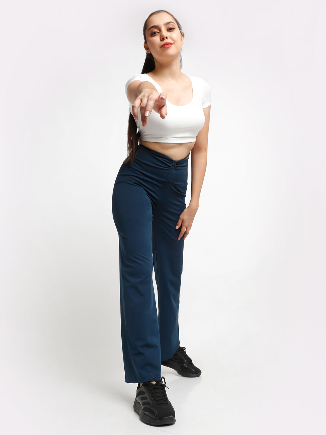 A female model wearing blue high waist tie up flared trousers and a white cropped top, standing against a plain background.