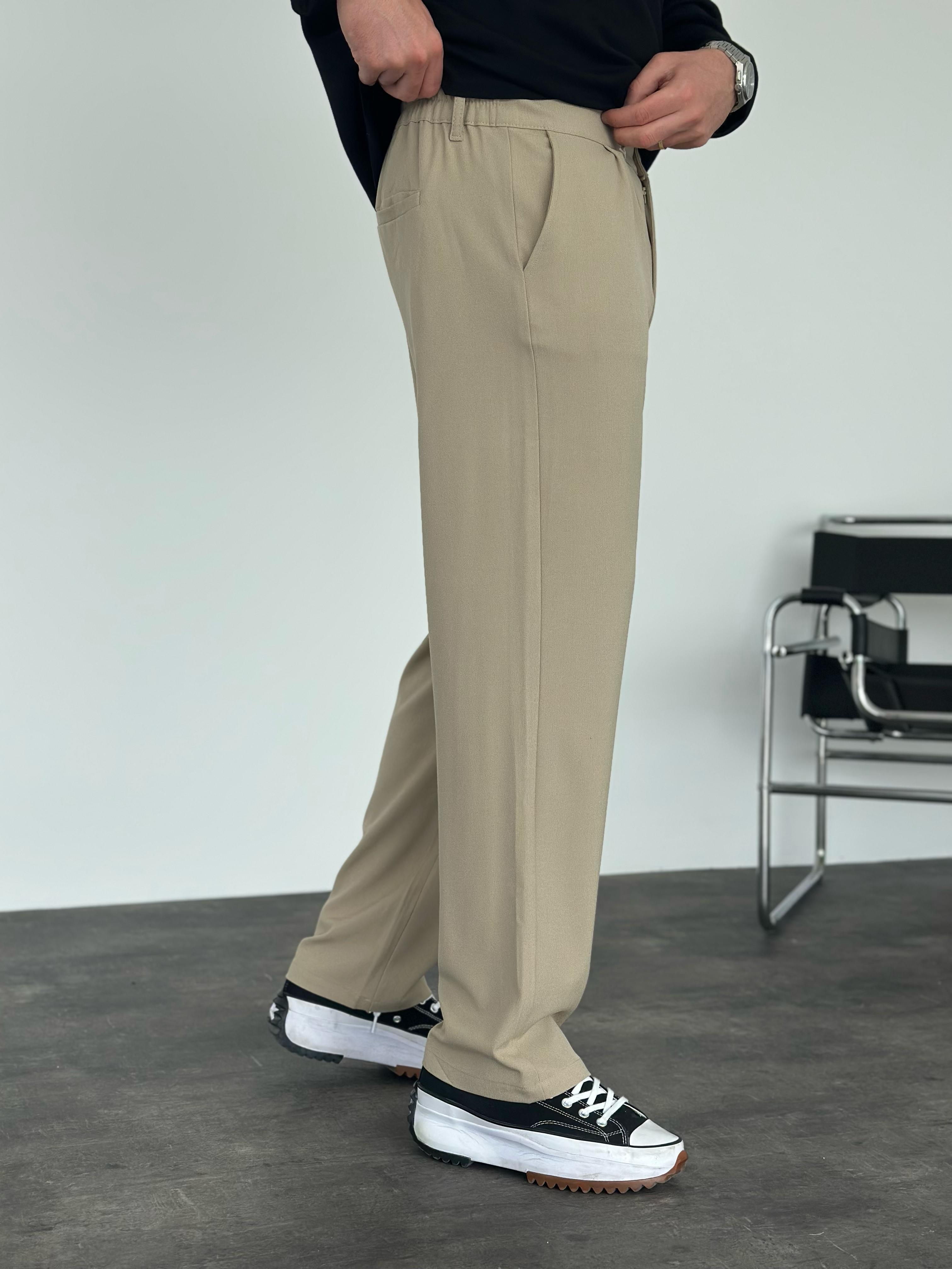 Person wearing beige pants and black shoes in a minimalistic setting