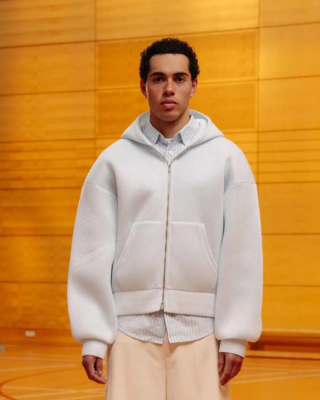 Person wearing a light gray hoodie over a patterned shirt with a yellow wall background