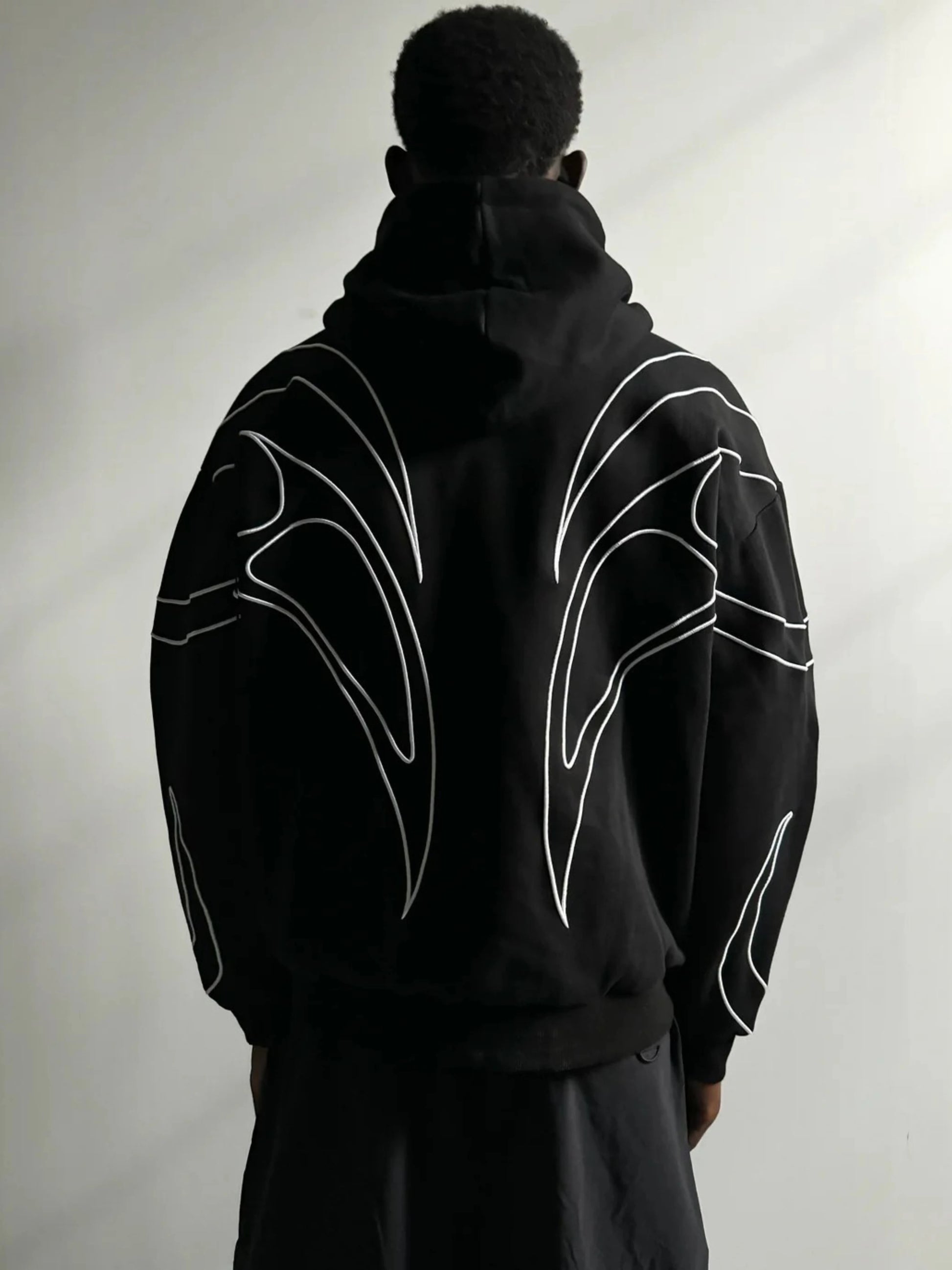 Person wearing a black hoodie with white abstract designs on the back against a light gray background