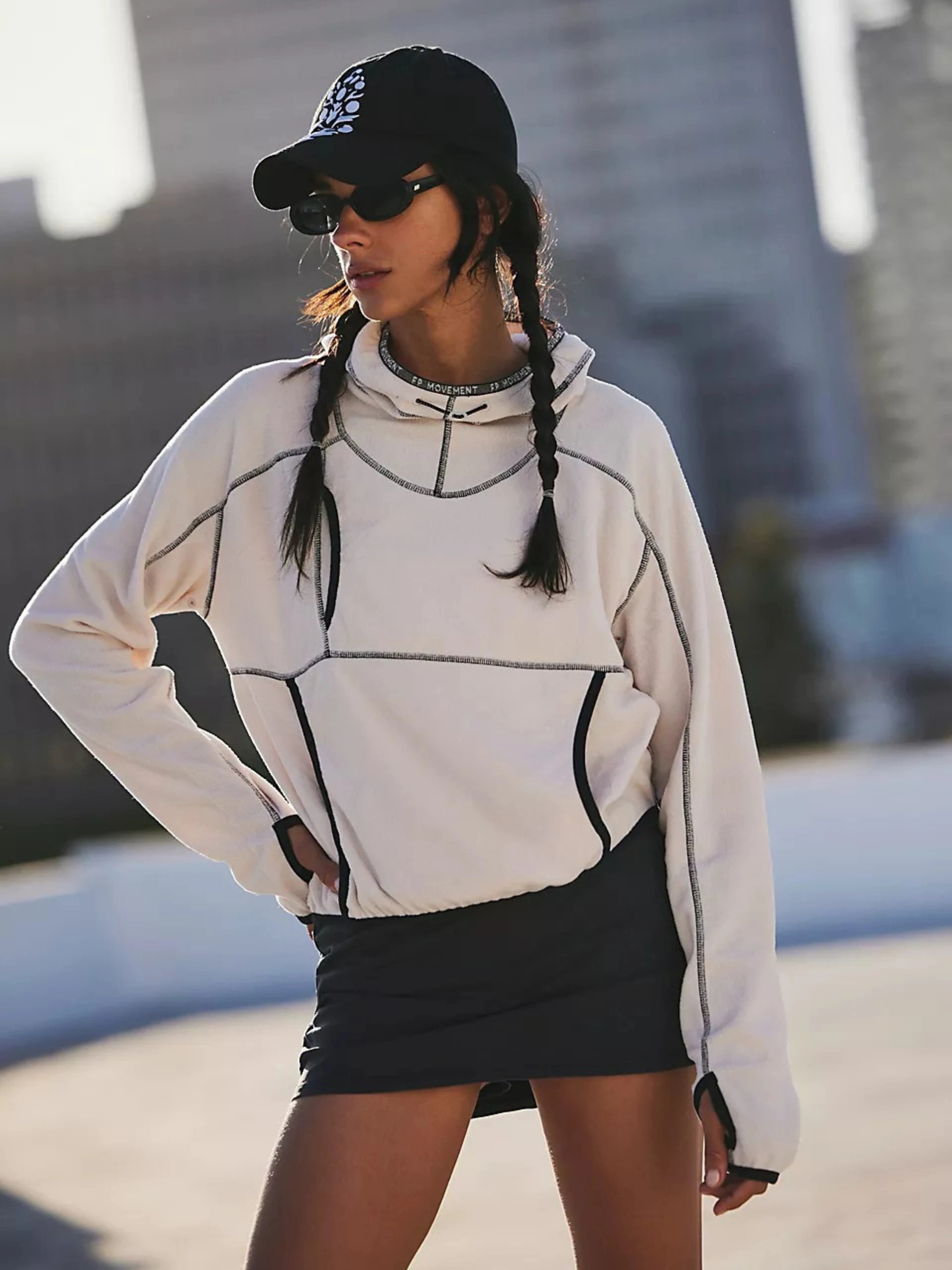 Woman wearing a light gray geometric-patterned hoodie and black skirt with a blurred urban background