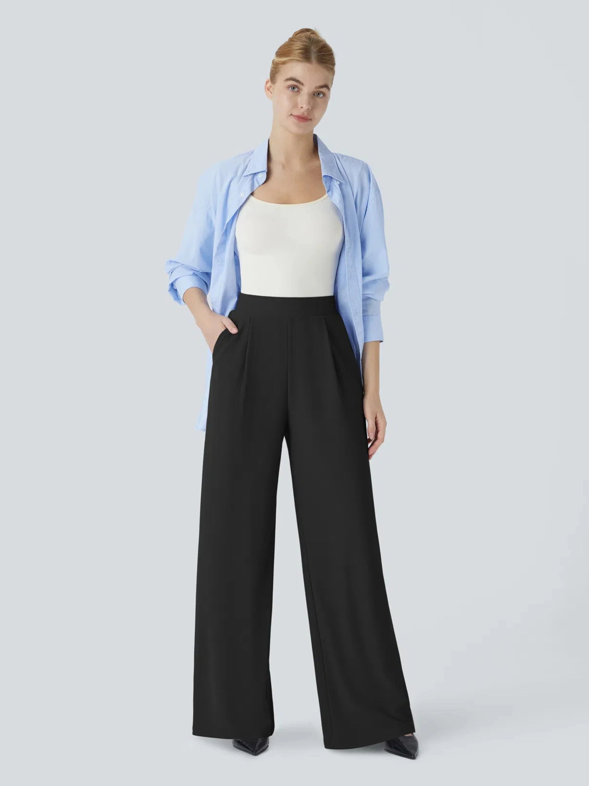 Woman wearing a light blue shirt, white top, and black wide-leg pants on a light gray background