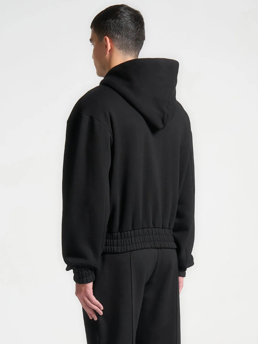 Person wearing a black hoodie and pants on a white background