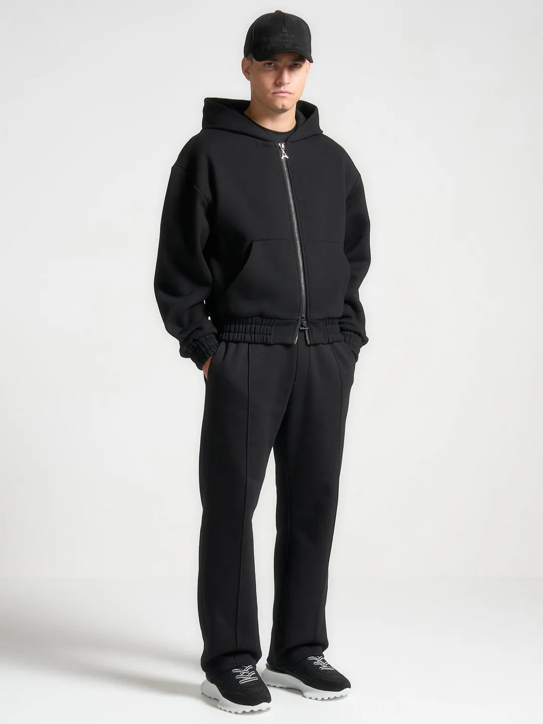 Person wearing a black tracksuit and cap on a white background