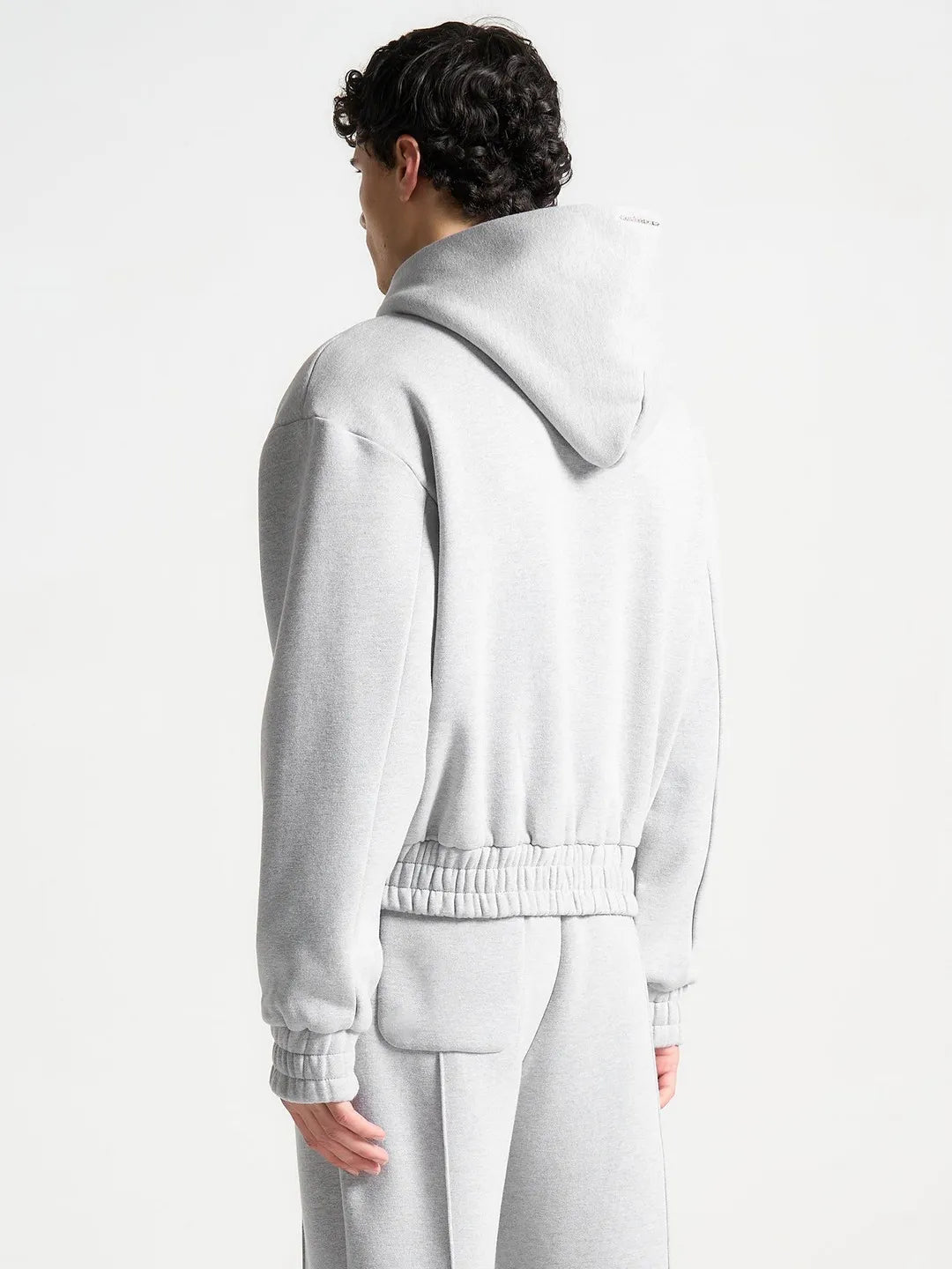 Person wearing a light gray hoodie and pants on a white background