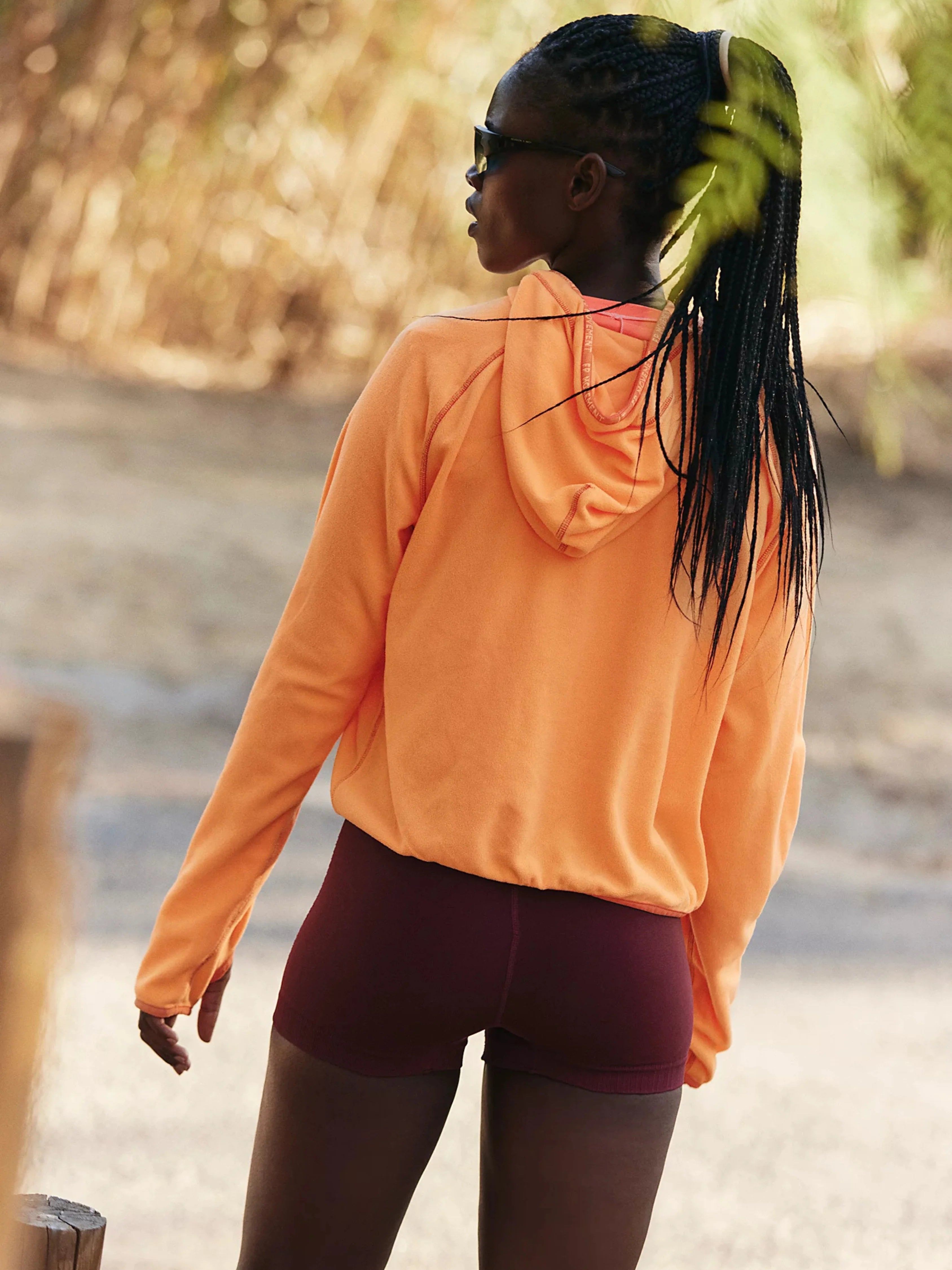 Person wearing an orange hoodie and maroon shorts outdoors
