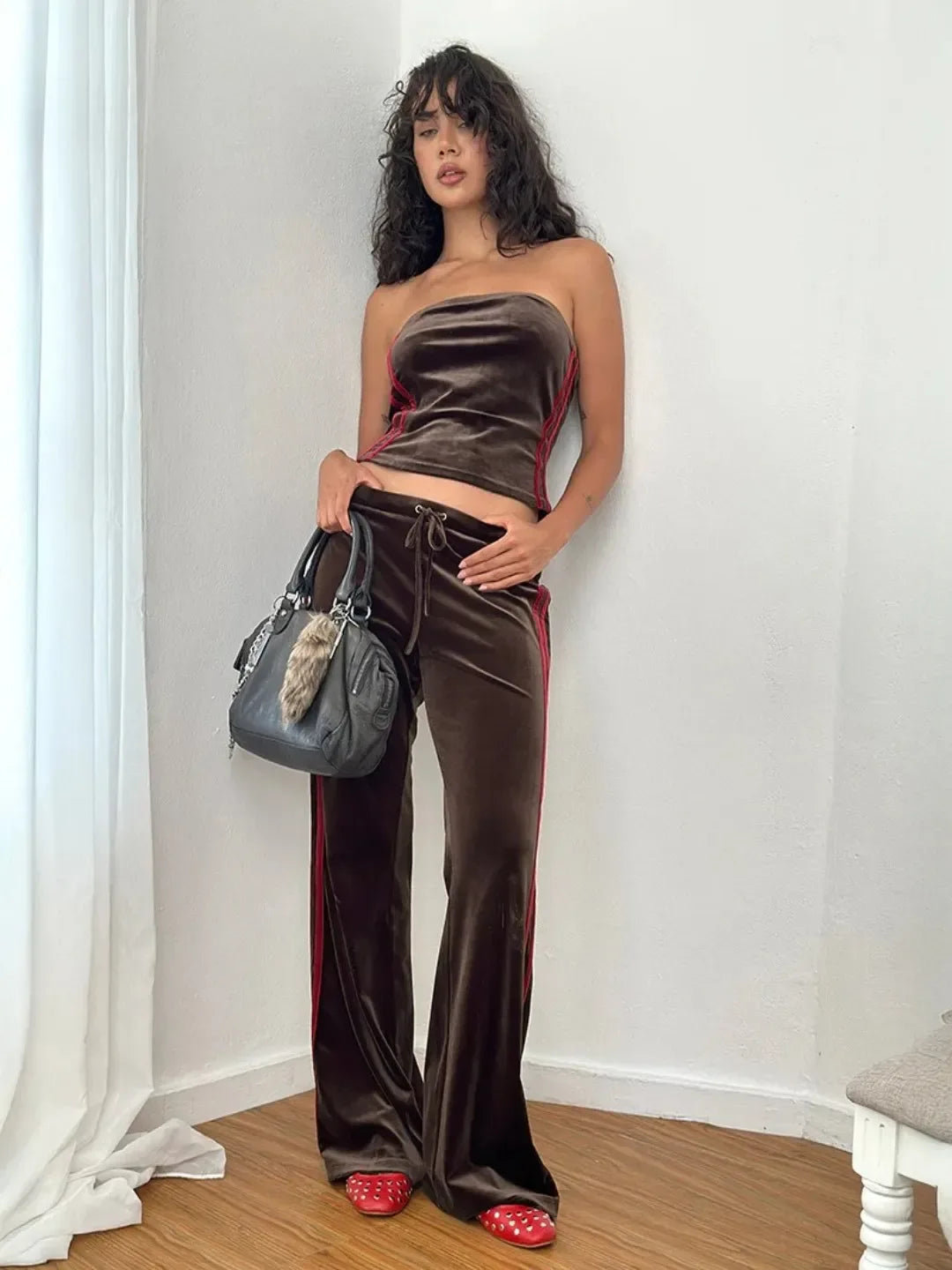 Woman in a strapless brown velvet top and wide-leg pants holding a gray handbag.