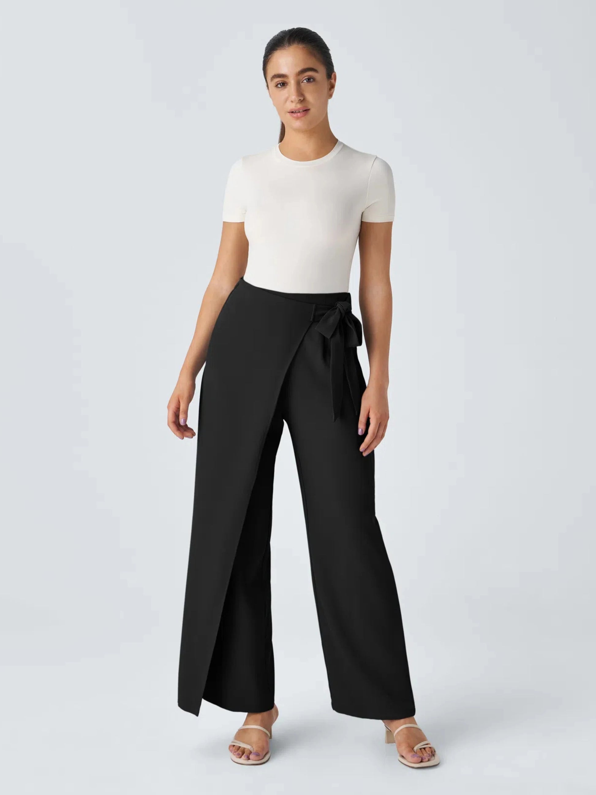 Woman wearing a white top and black wide-leg pants on a plain background