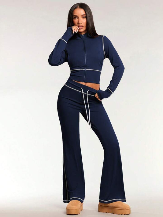 A woman standing and posing in a navy blue tracksuit, consisting of a zip-up jacket and leggings, with long sleeves and a pair of shoes visible.