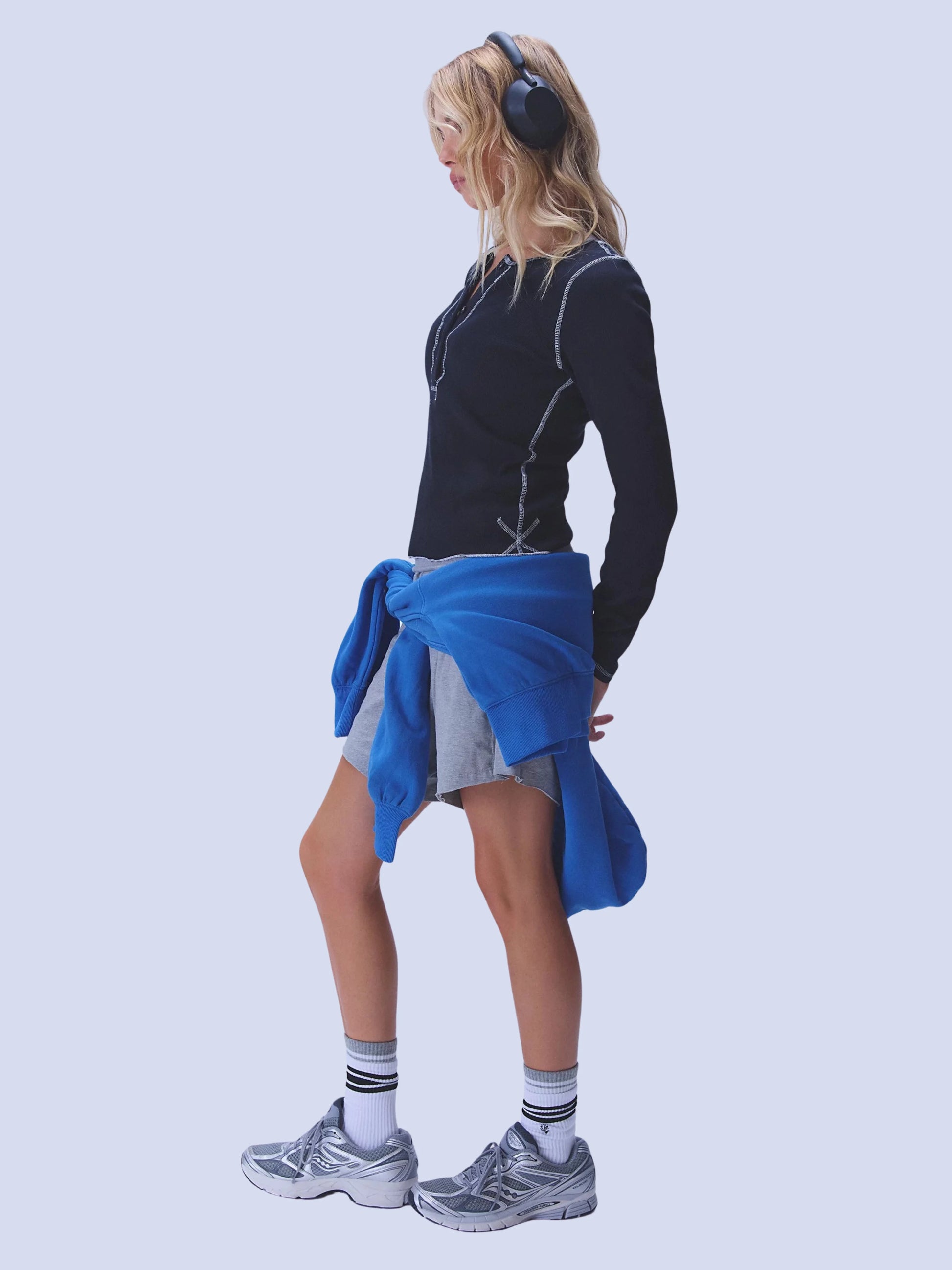 Person wearing a black long-sleeve top, gray shorts, and gray sneakers with a blue towel over their shoulder on a light gray background.