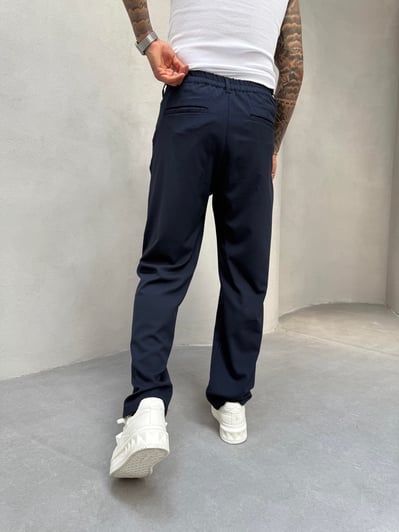 Person wearing navy pants and white sneakers against a plain background