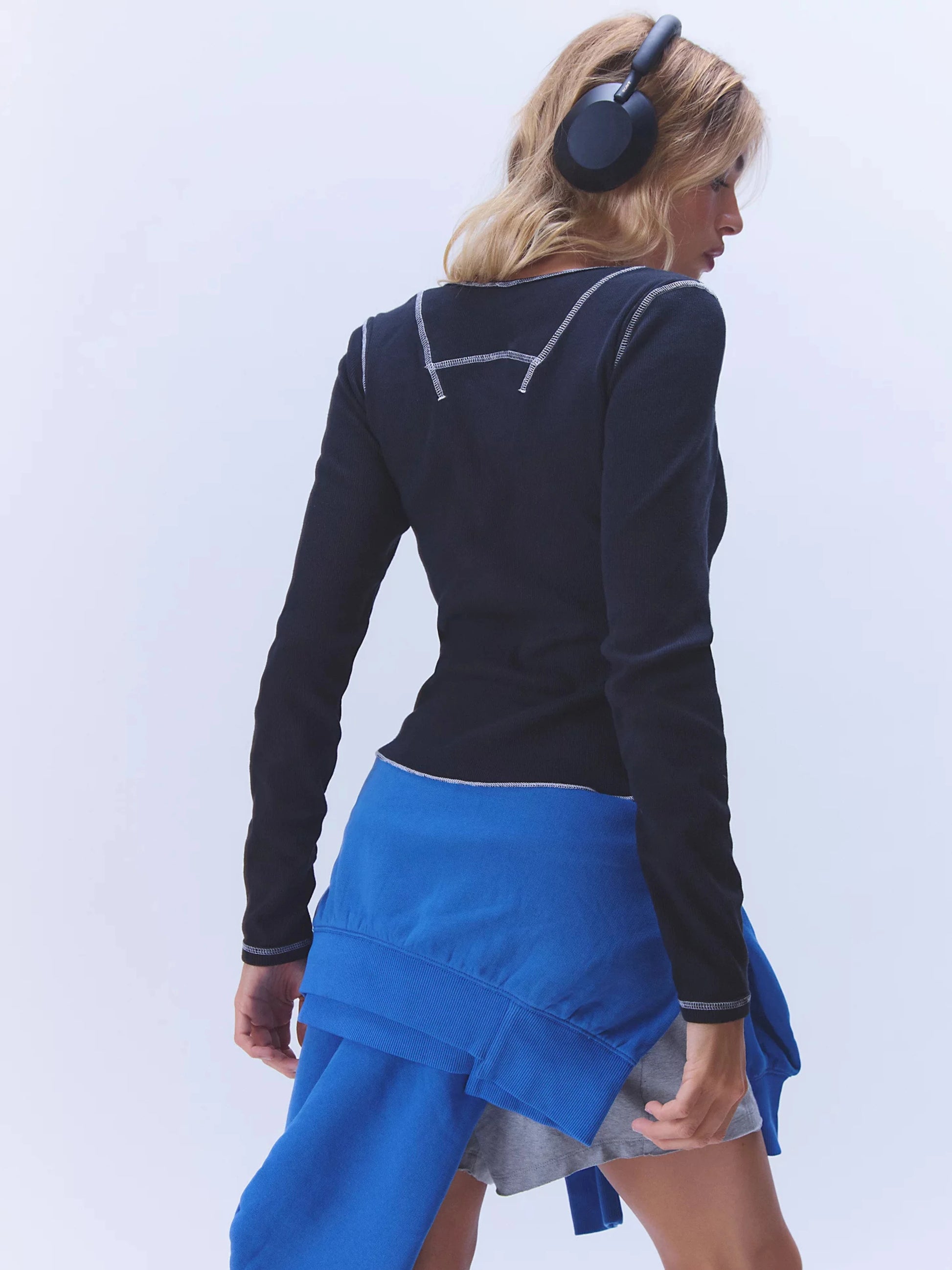 Person wearing a black long-sleeve top and blue skirt on a light gray background