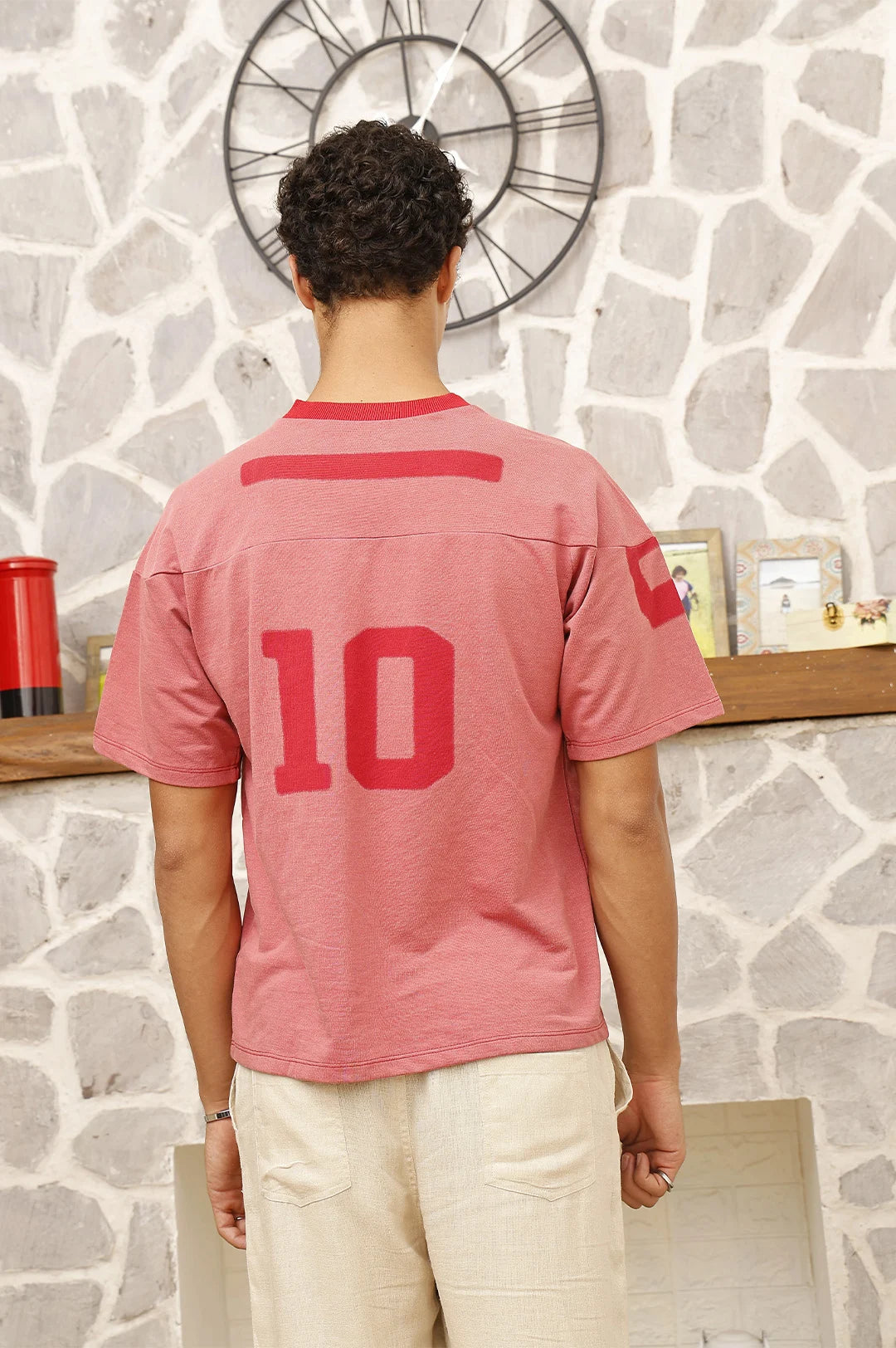 Person wearing a red sports jersey with number 10, standing in front of a stone wall with a clock.