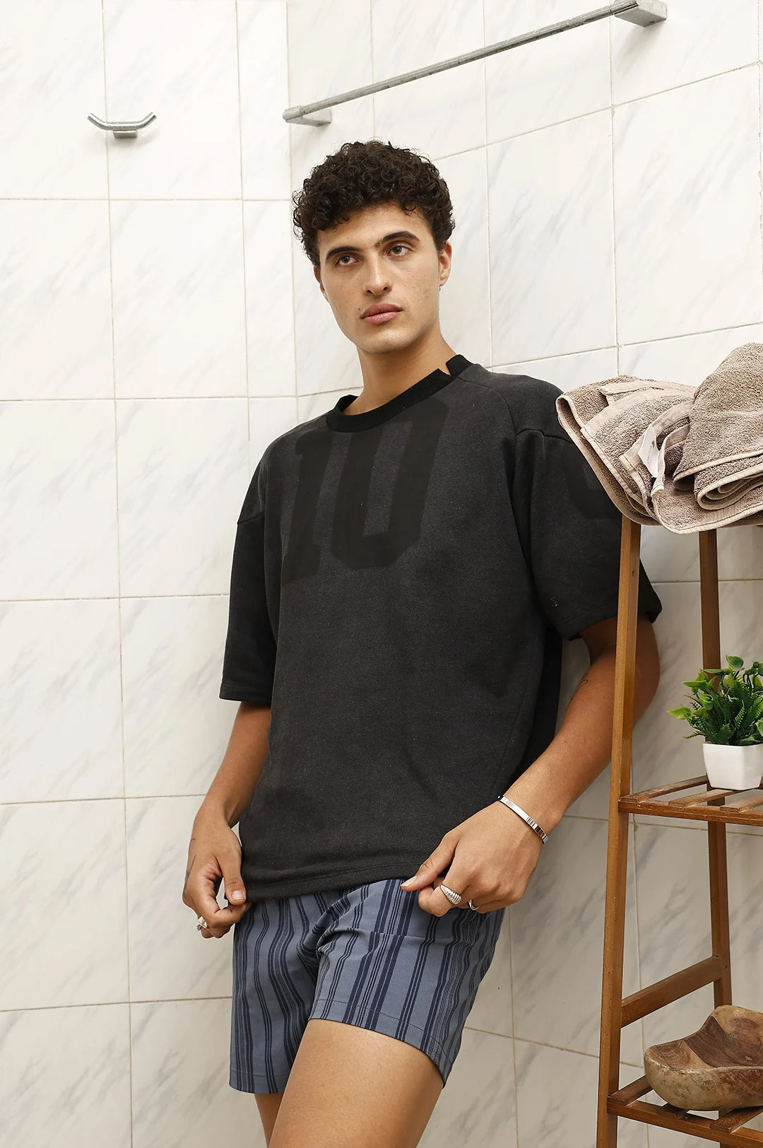 Man wearing a black t-shirt and striped shorts in a bathroom.
