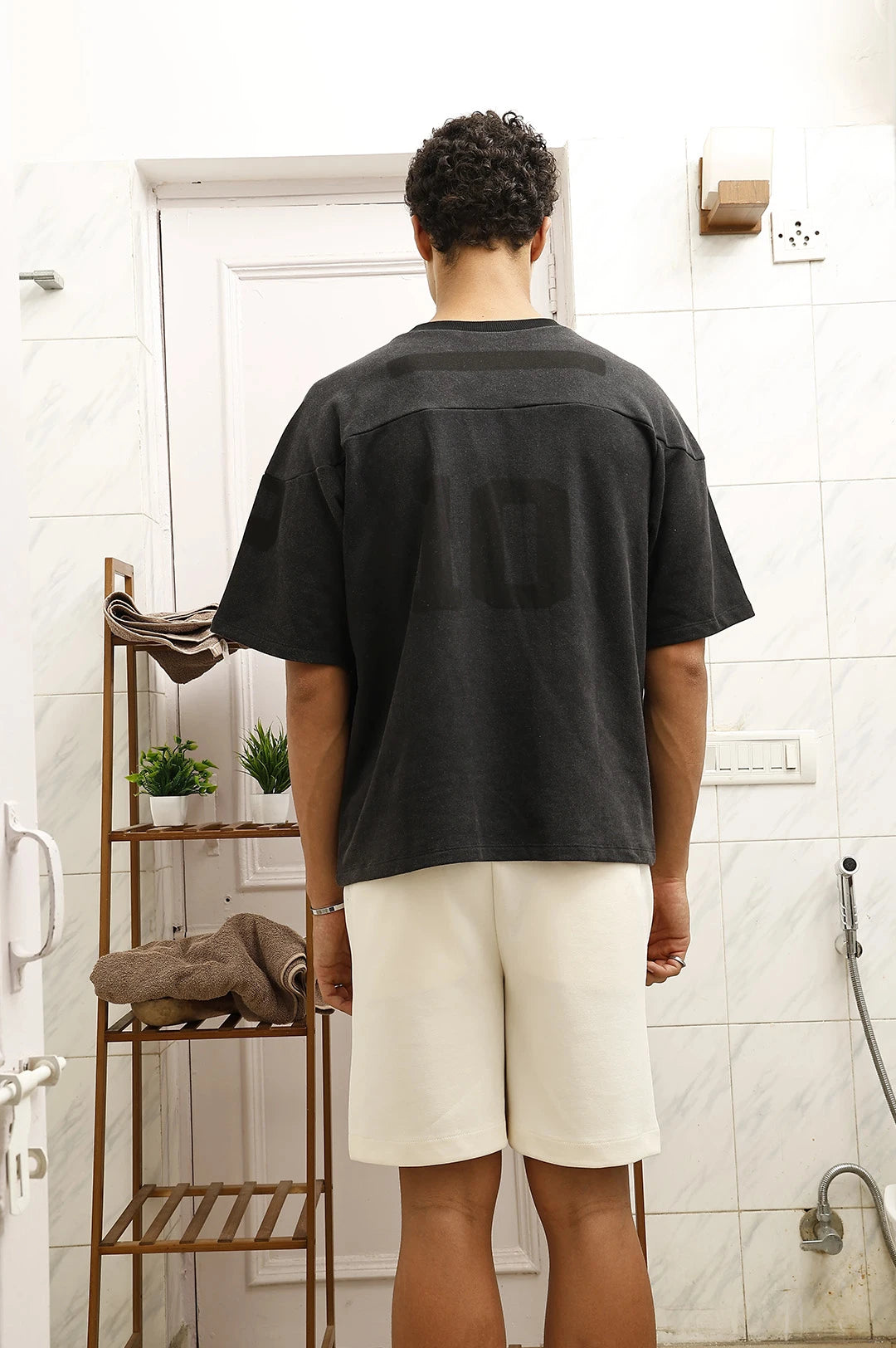 Person wearing a black t-shirt and white shorts standing in a bathroom.