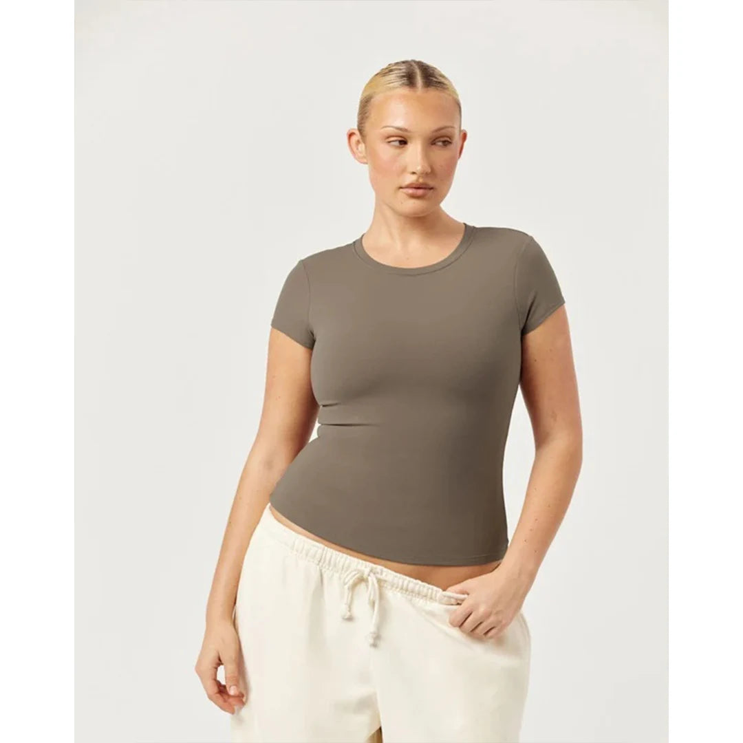 Woman wearing a brown t-shirt and white pants on a light gray background