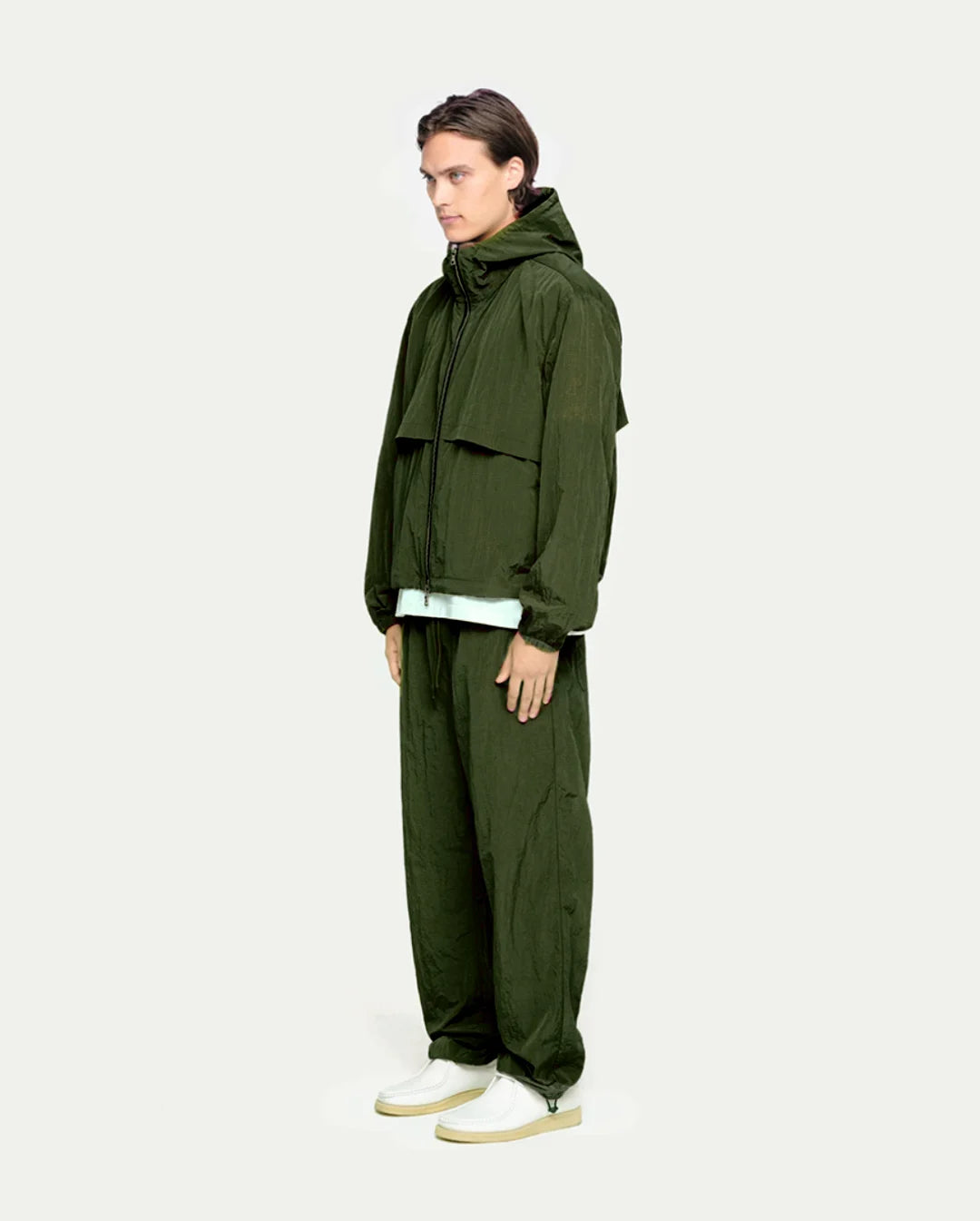 Person wearing a olive raincoat and pants on a white background