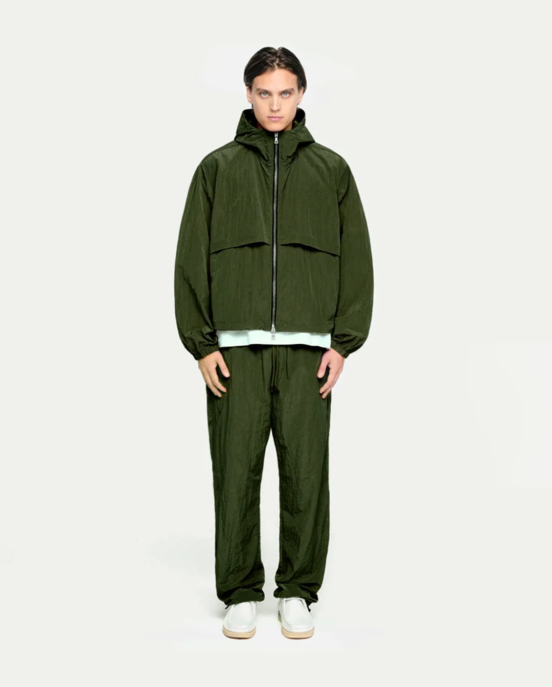 Person wearing an olive raincoat and pants on a white background