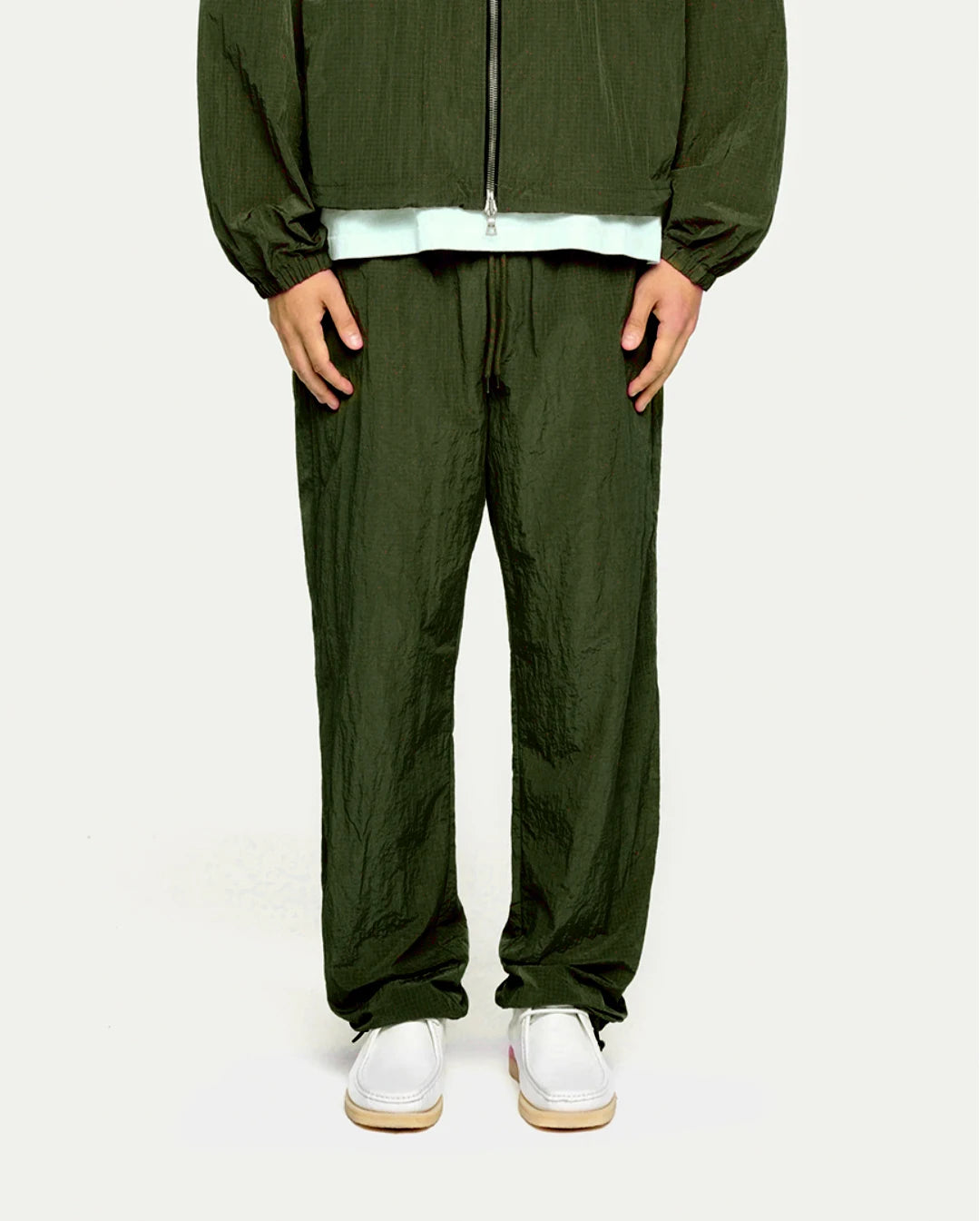 Person wearing a olive tracksuit with white shoes on a plain background