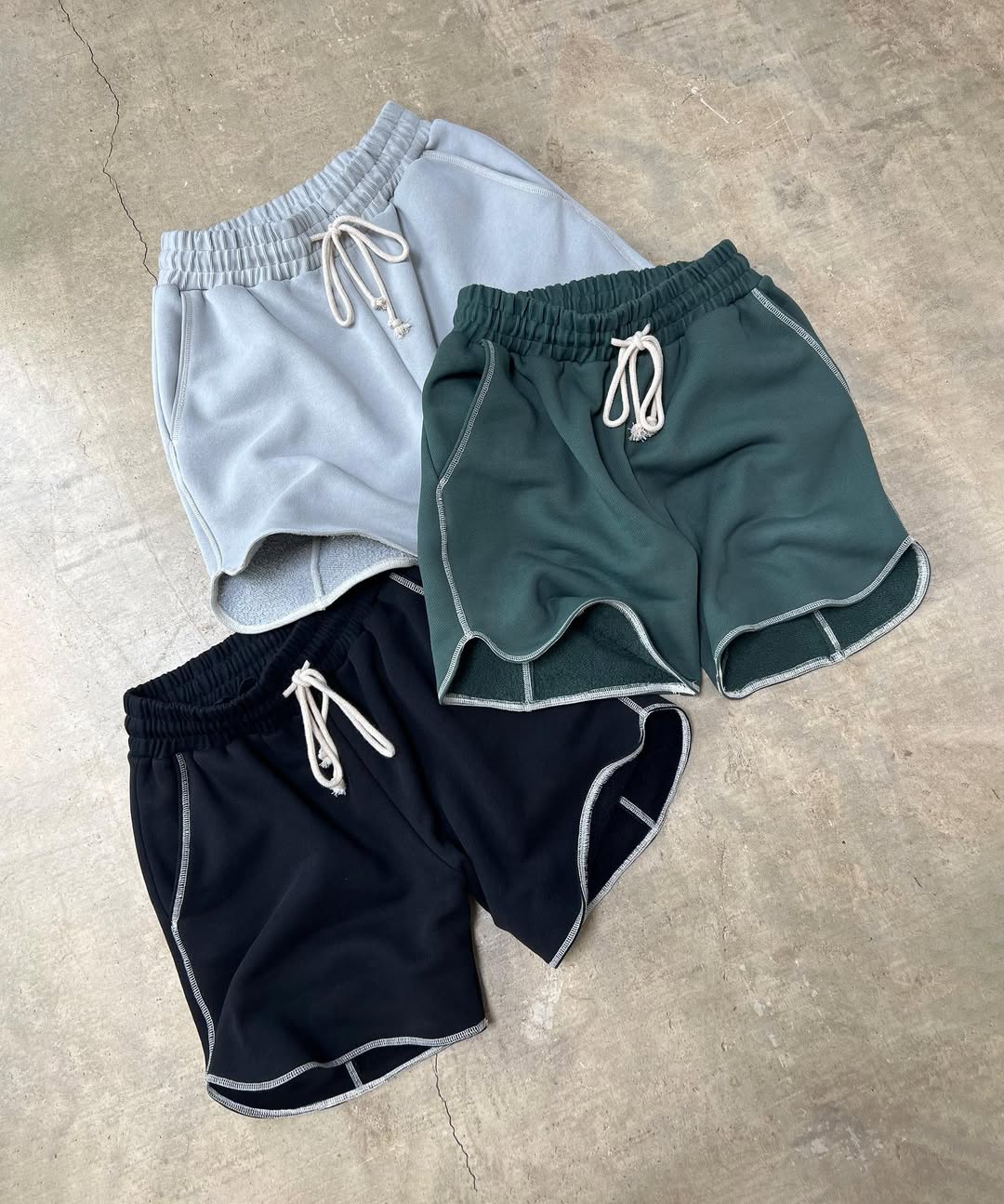 A set of three men's overlock running shorts in gray, green, and black colors, displayed flat on a surface.