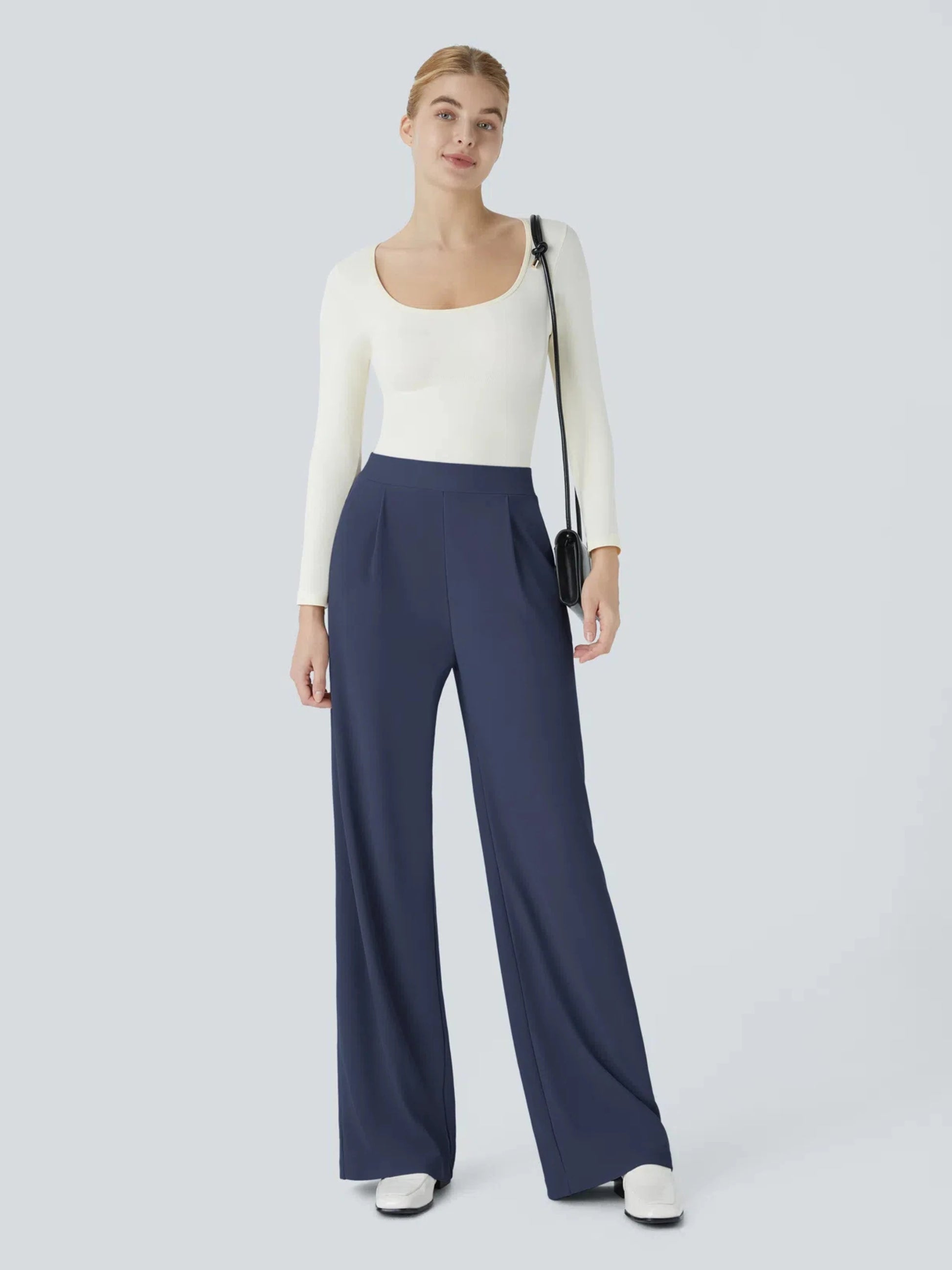 Woman wearing a white top and navy pants on a light gray background