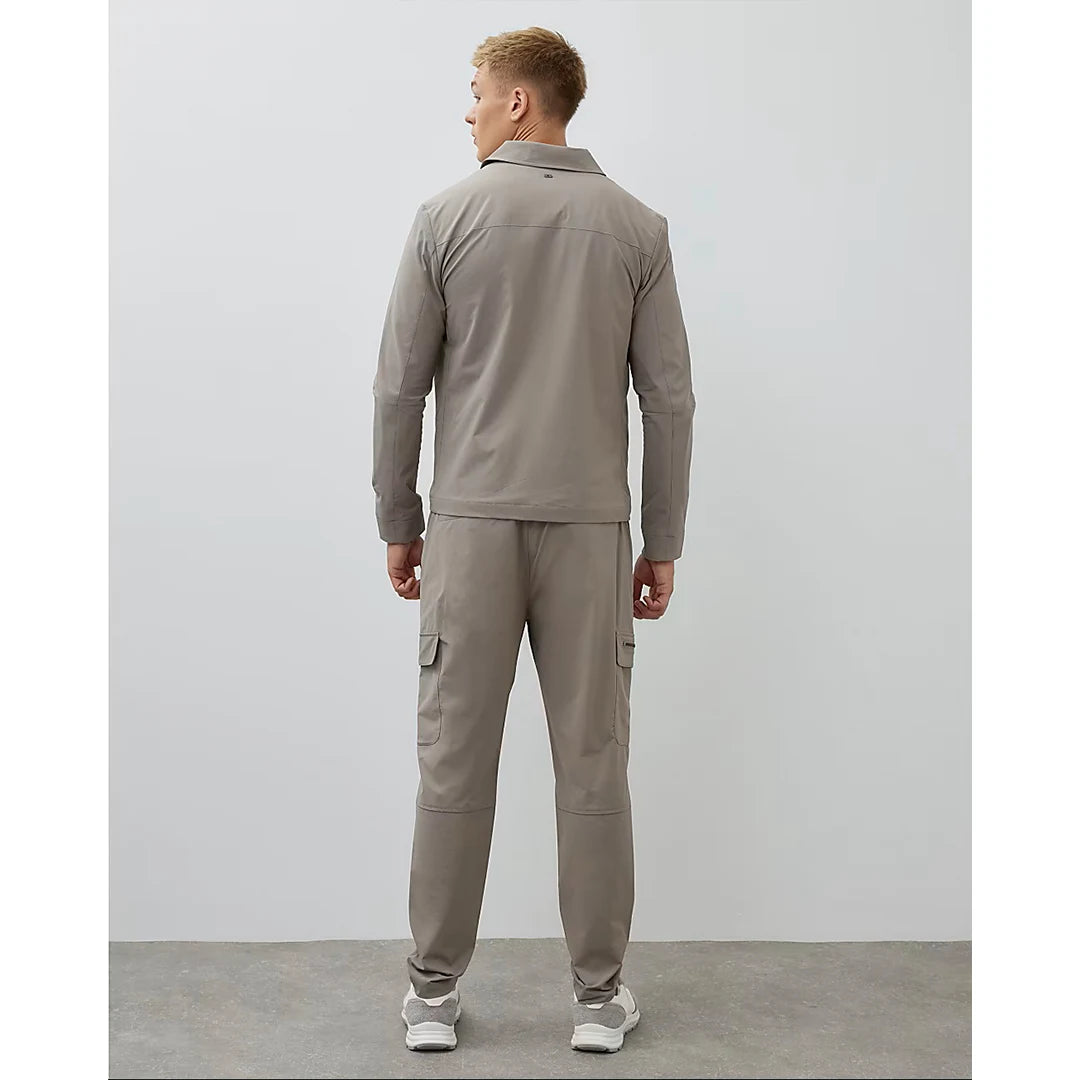 Man wearing a beige tracksuit standing against a white wall