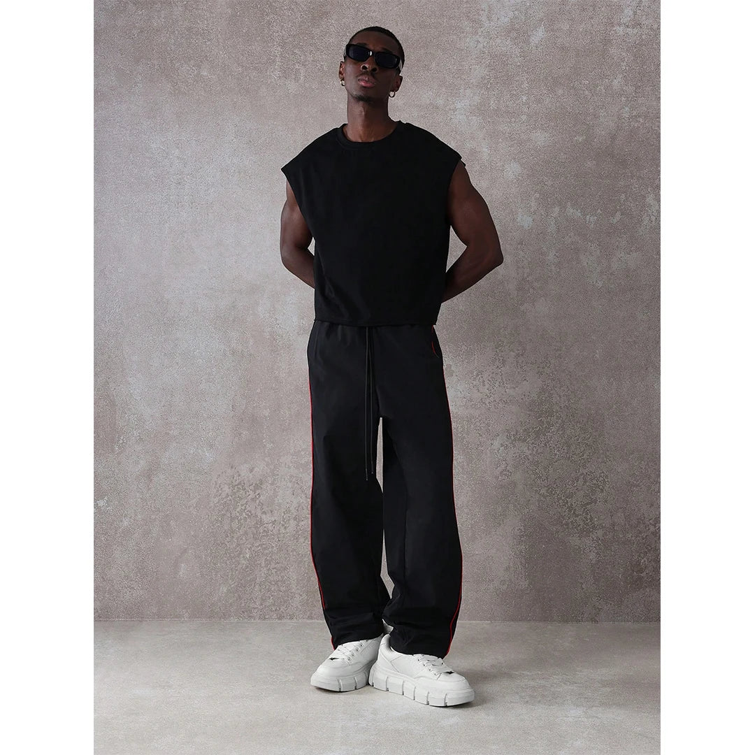 Man wearing a black sleeveless top and pants with white sneakers against a gray concrete wall.