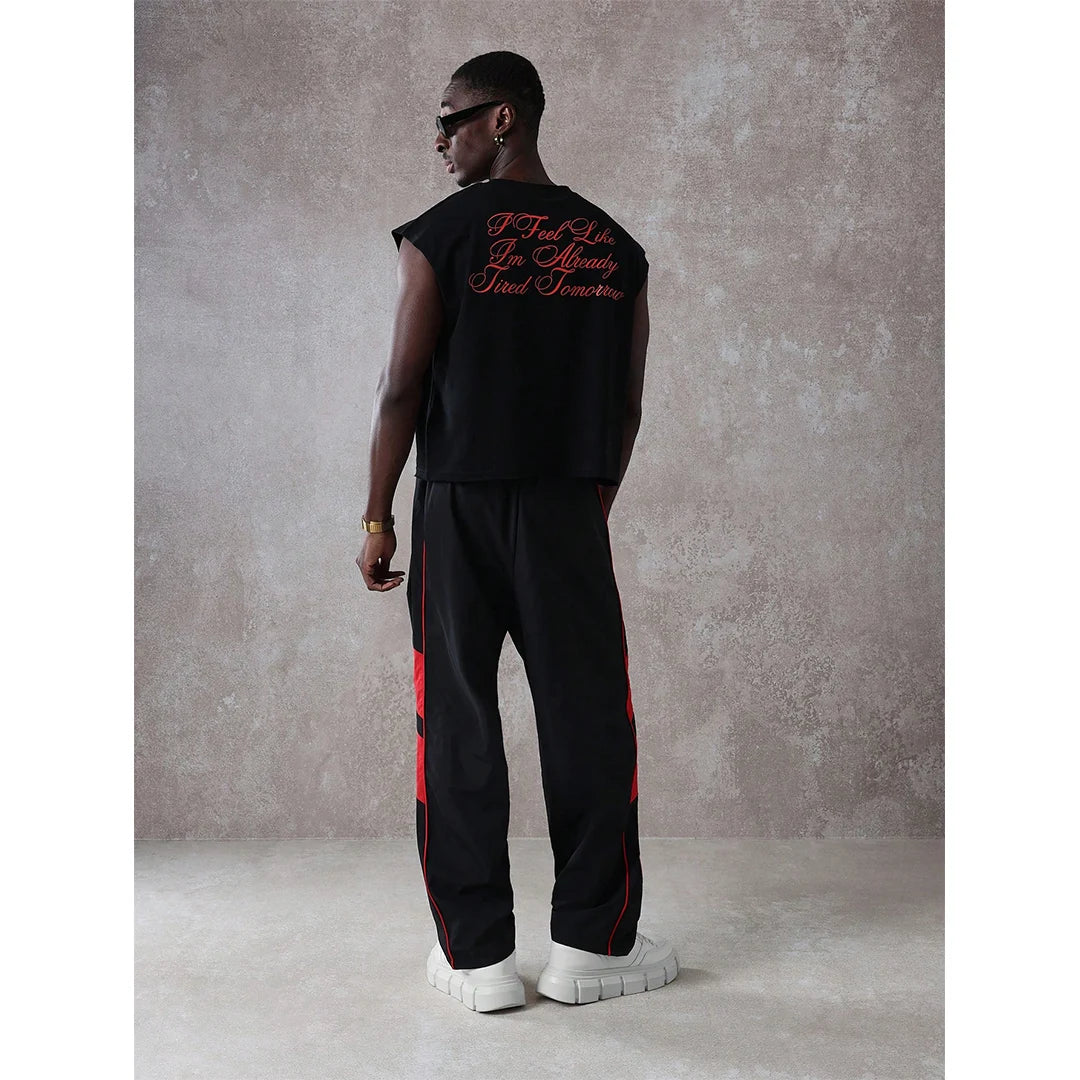 Man wearing a black sleeveless top and pants with red accents against a gray background