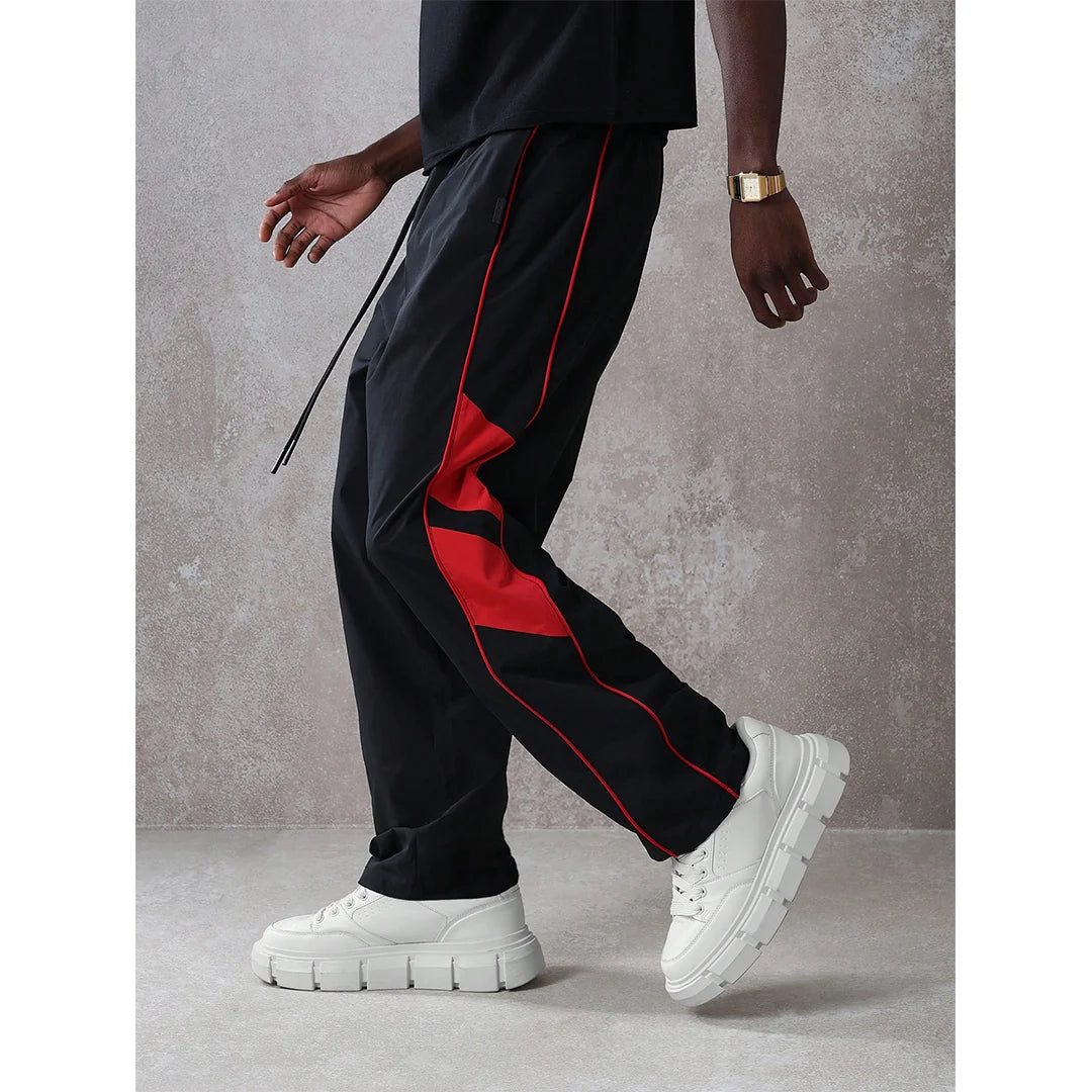 Person wearing black pants with red stripes and white sneakers on a gray background
