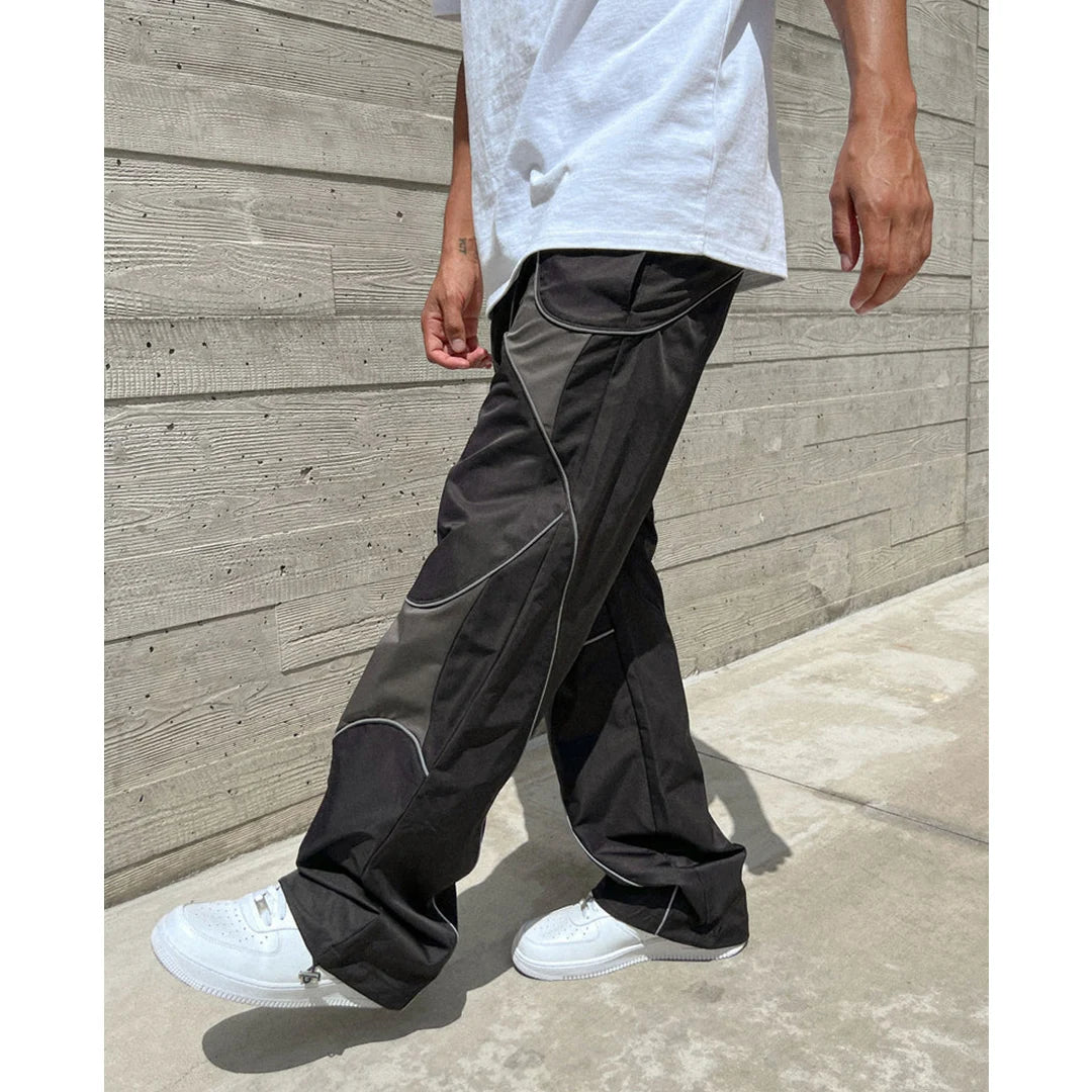 Person wearing black pants with white accents against a wooden wall.