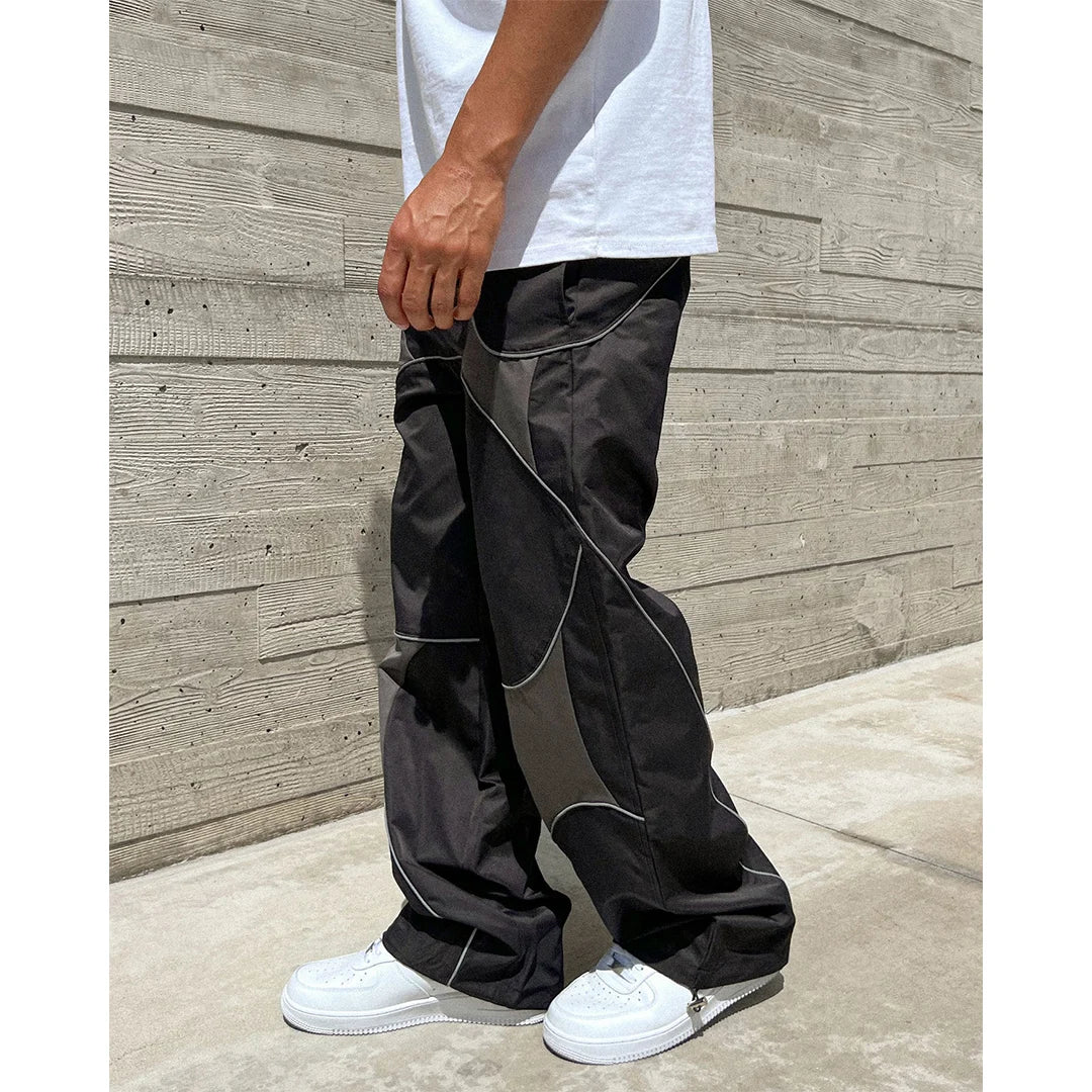 Person wearing black pants with white trim against a wooden wall.
