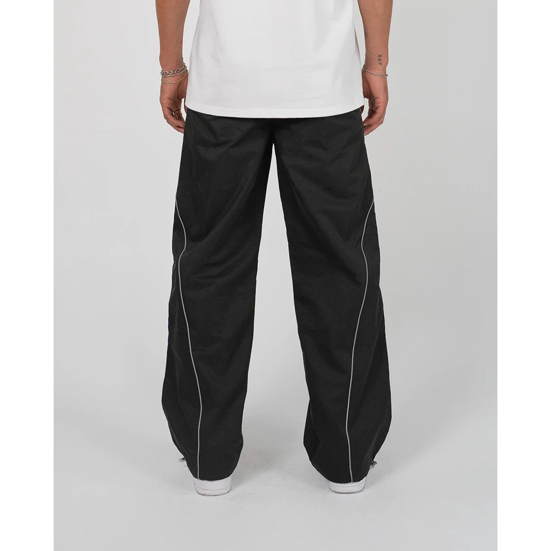 Person wearing black pants with white piping on a plain background