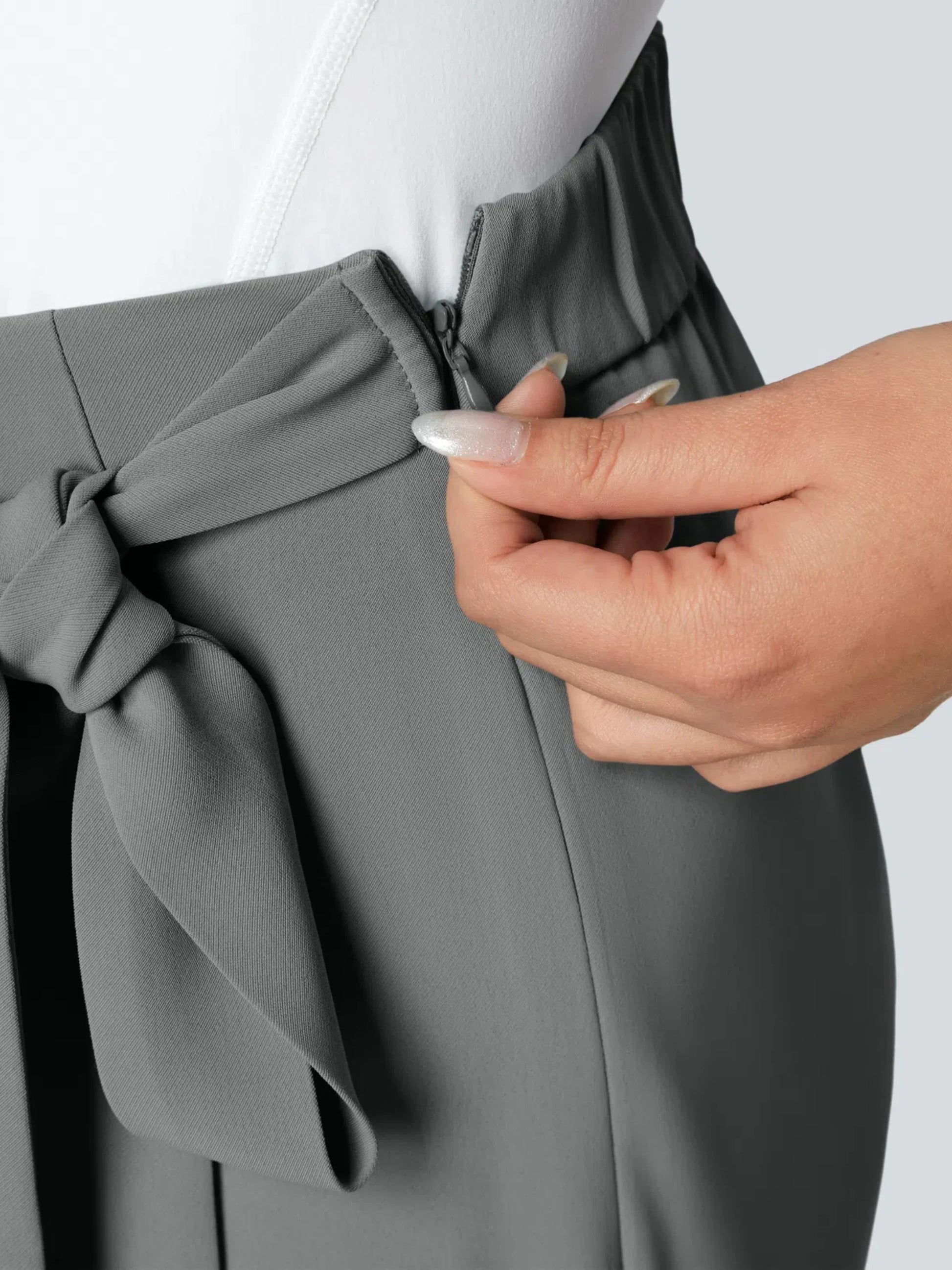 Person adjusting a gray garment with a bow detail on a plain background