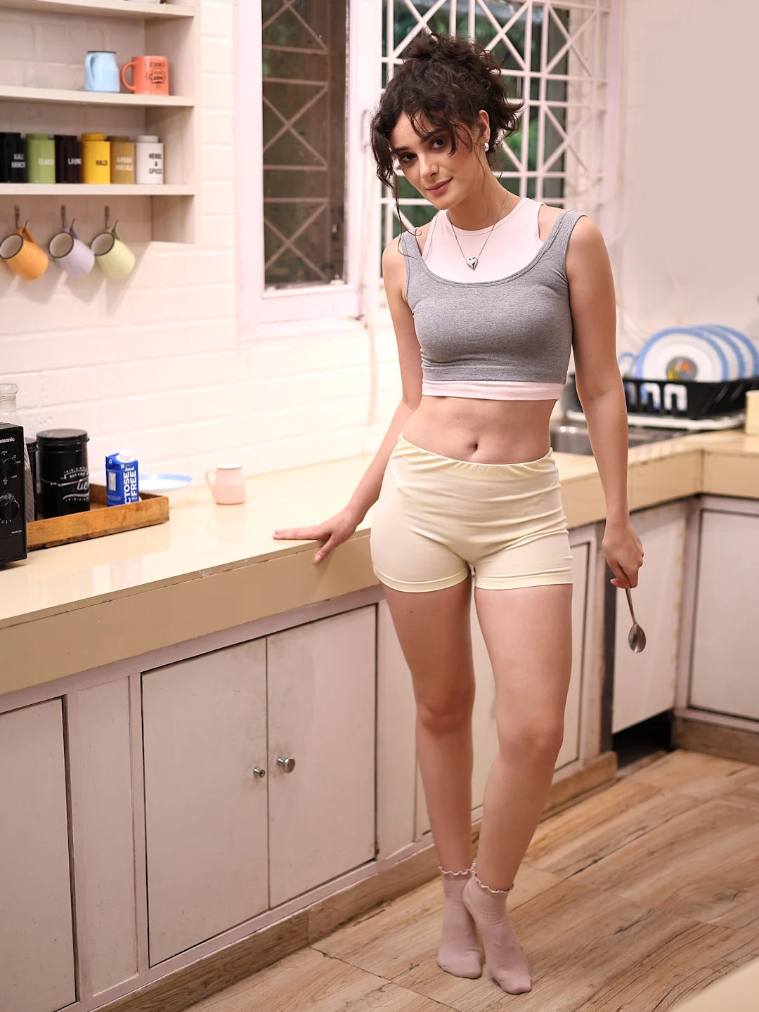 Woman standing in a kitchen wearing a gray sports bra and beige shorts.