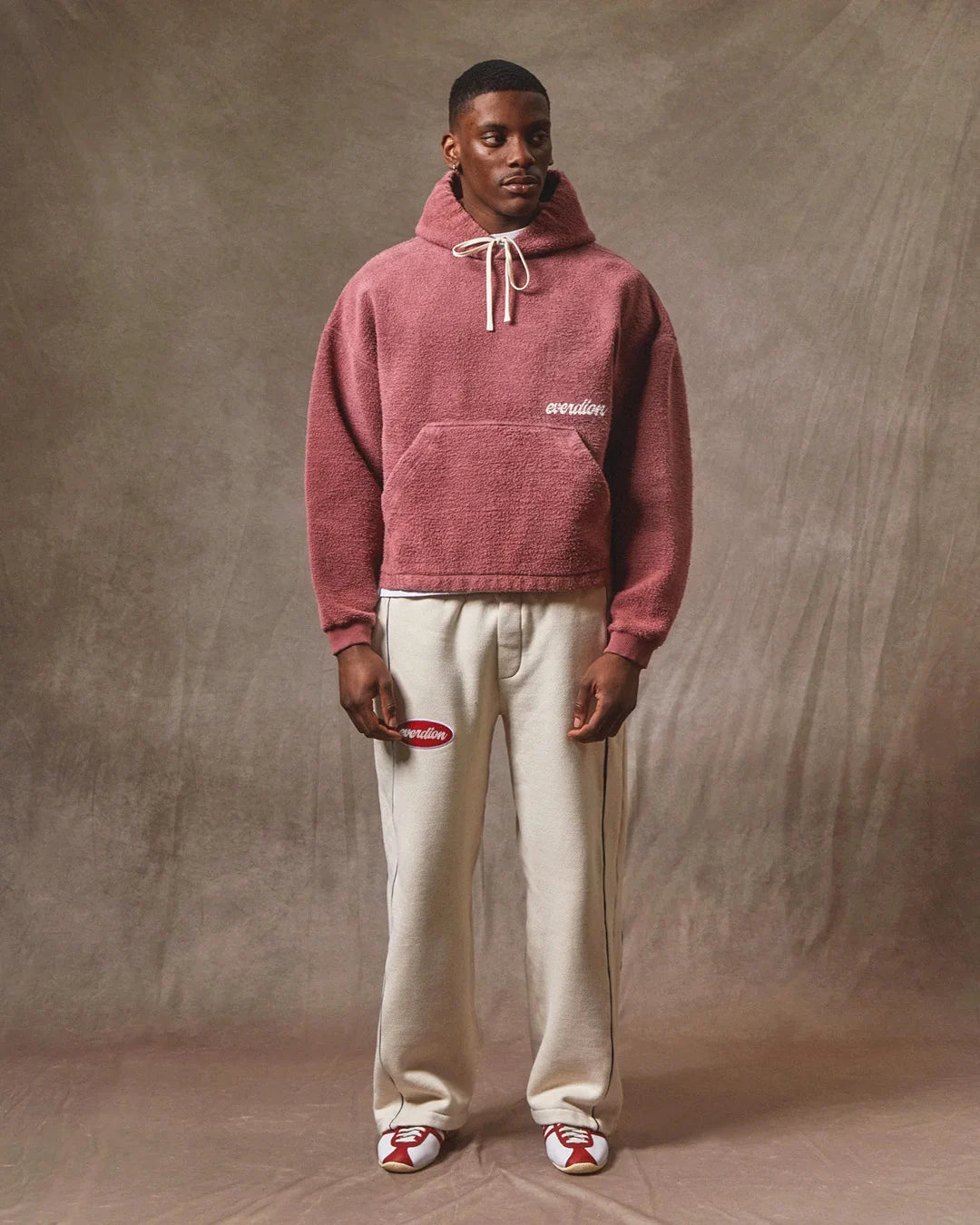 Person wearing a red hoodie and white pants against a brown background