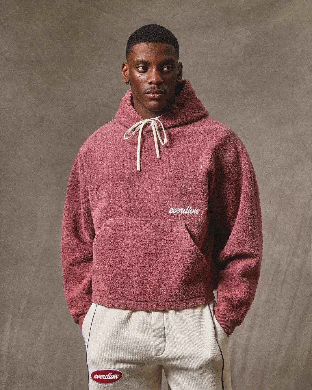 Man wearing a maroon hoodie with a logo on a brown background