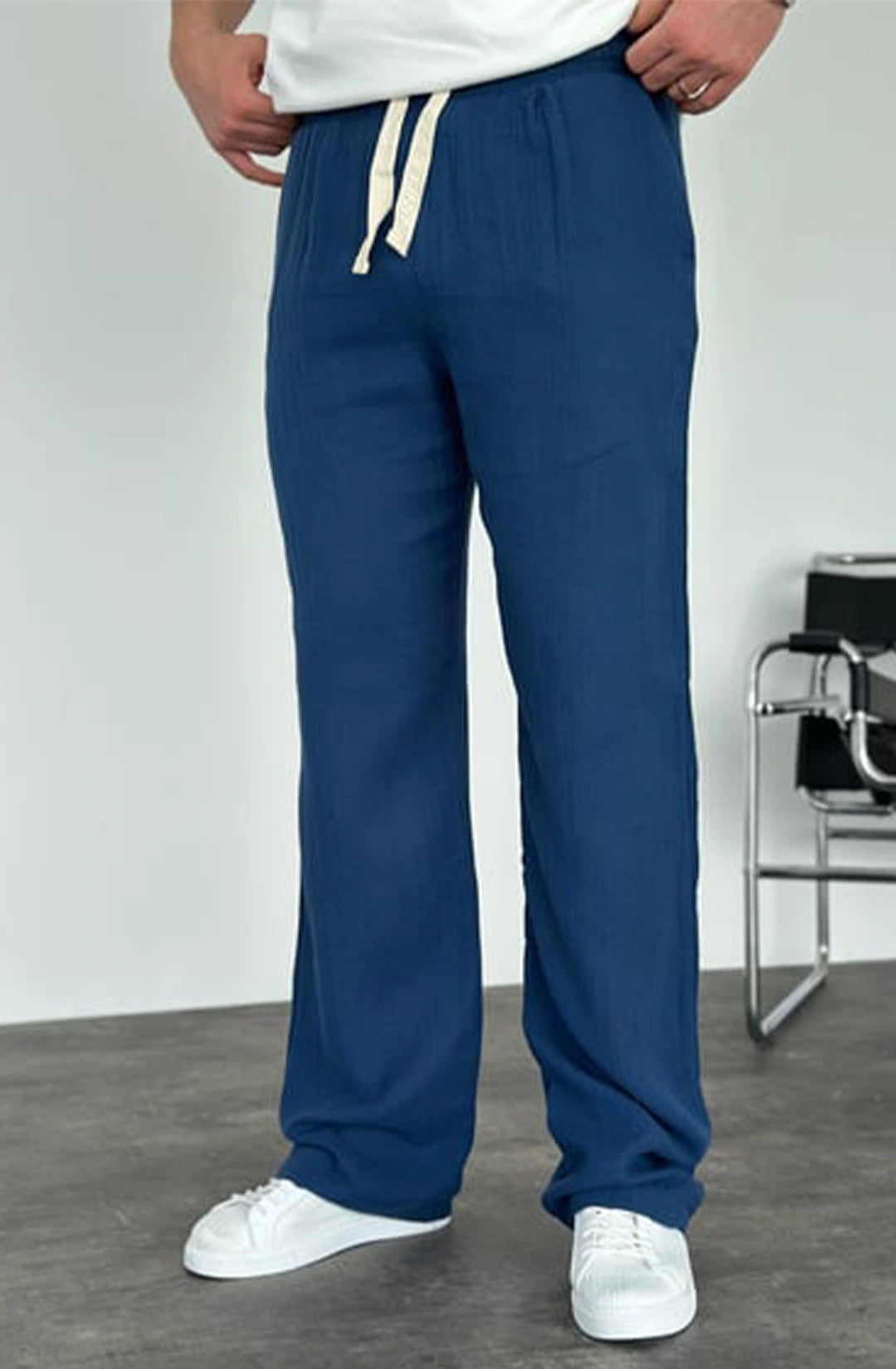 Person wearing blue pants with white drawstring and white shoes on a plain background