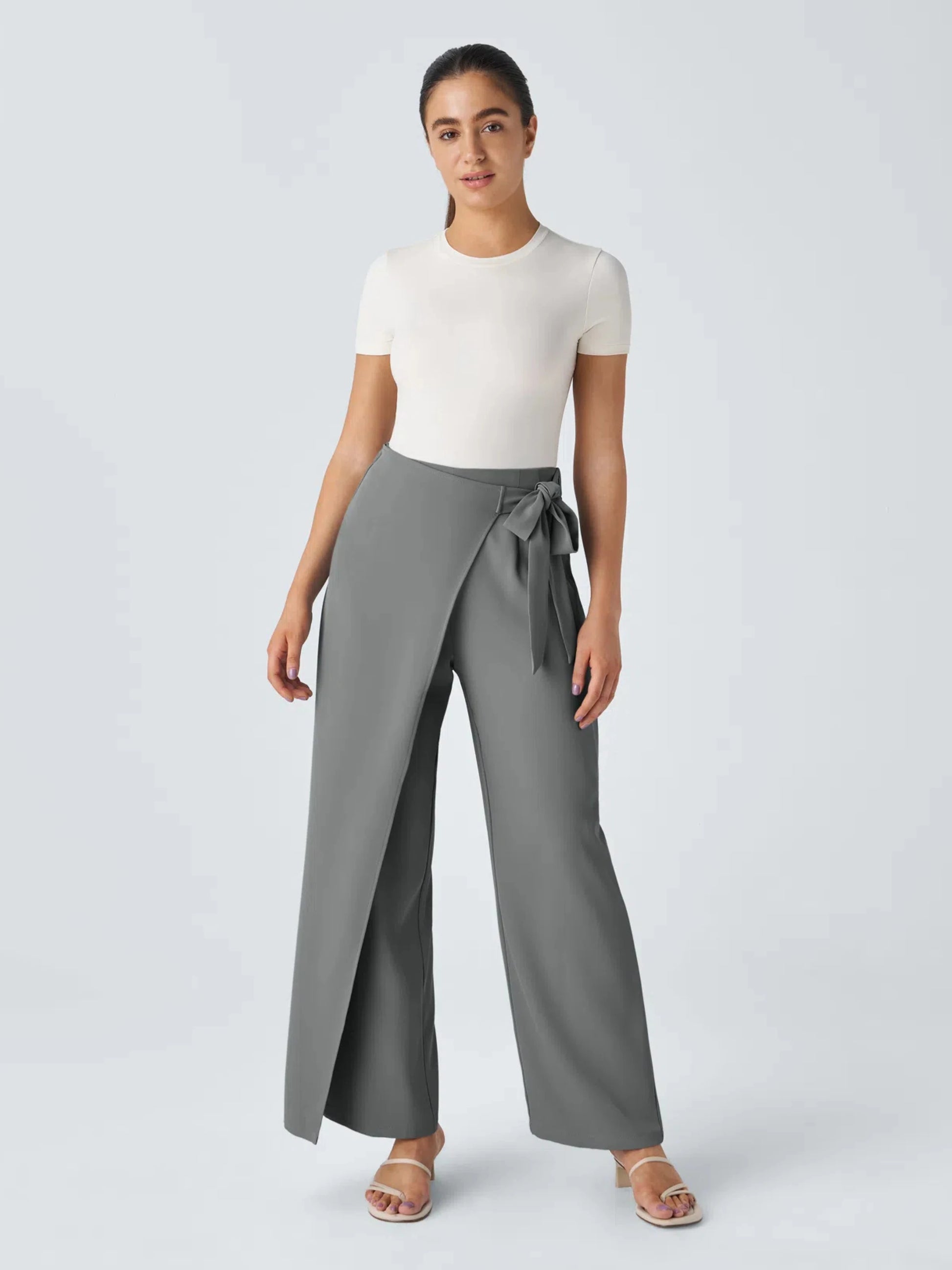 Woman wearing a white top and gray wide-leg pants with a belt on a light gray background