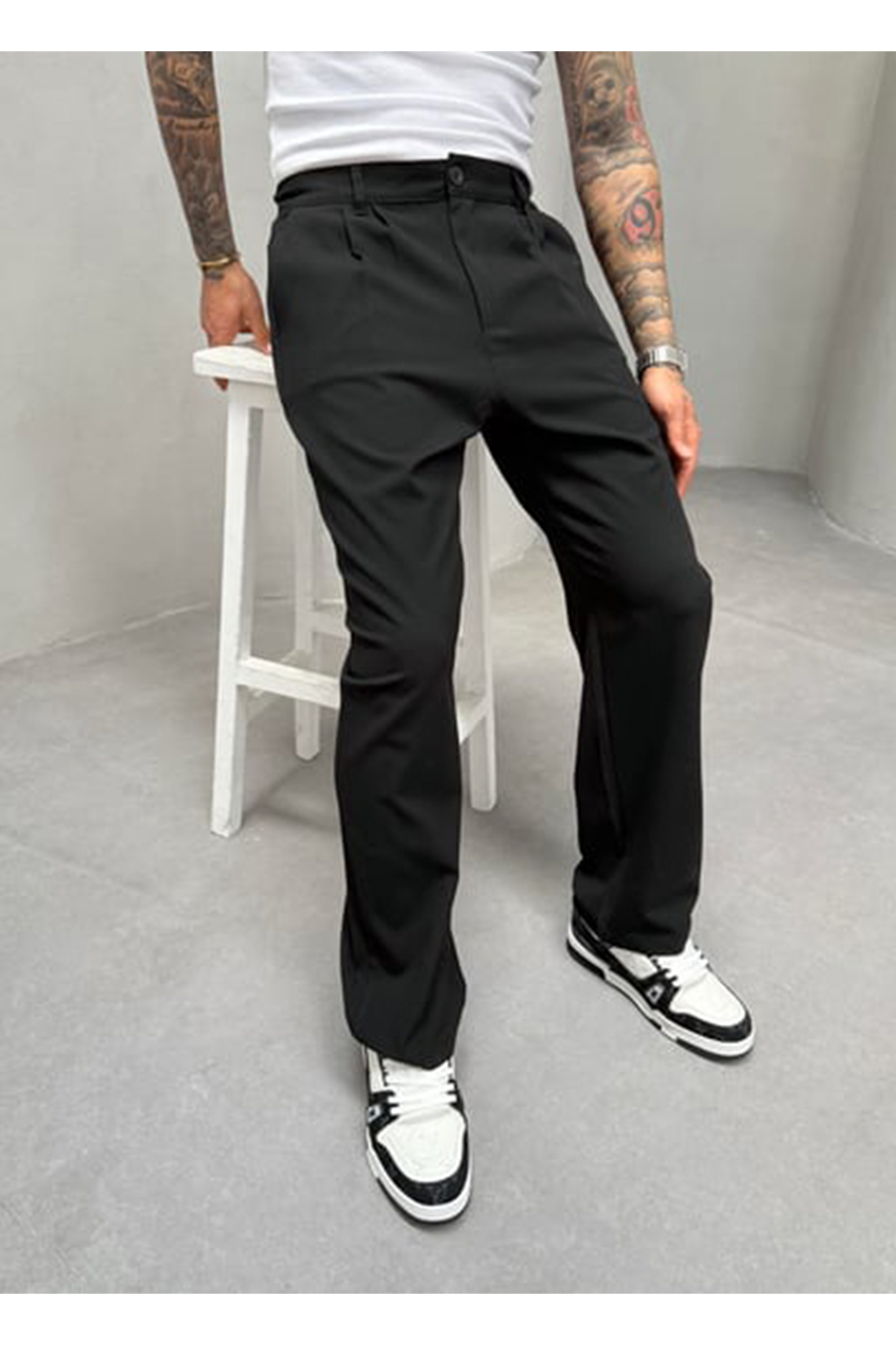 A person wearing black pants and white sneakers on a gray floor with a white stool.