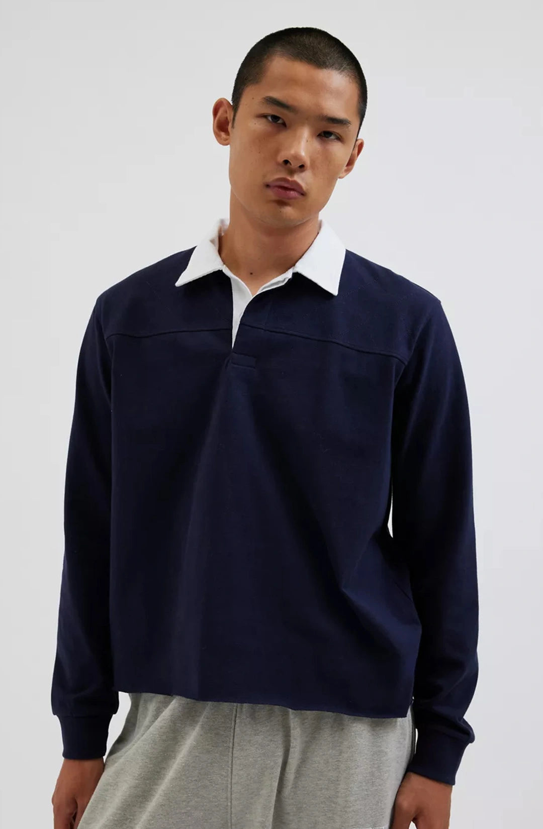 Man wearing a navy long-sleeve shirt over a white collared shirt on a plain background