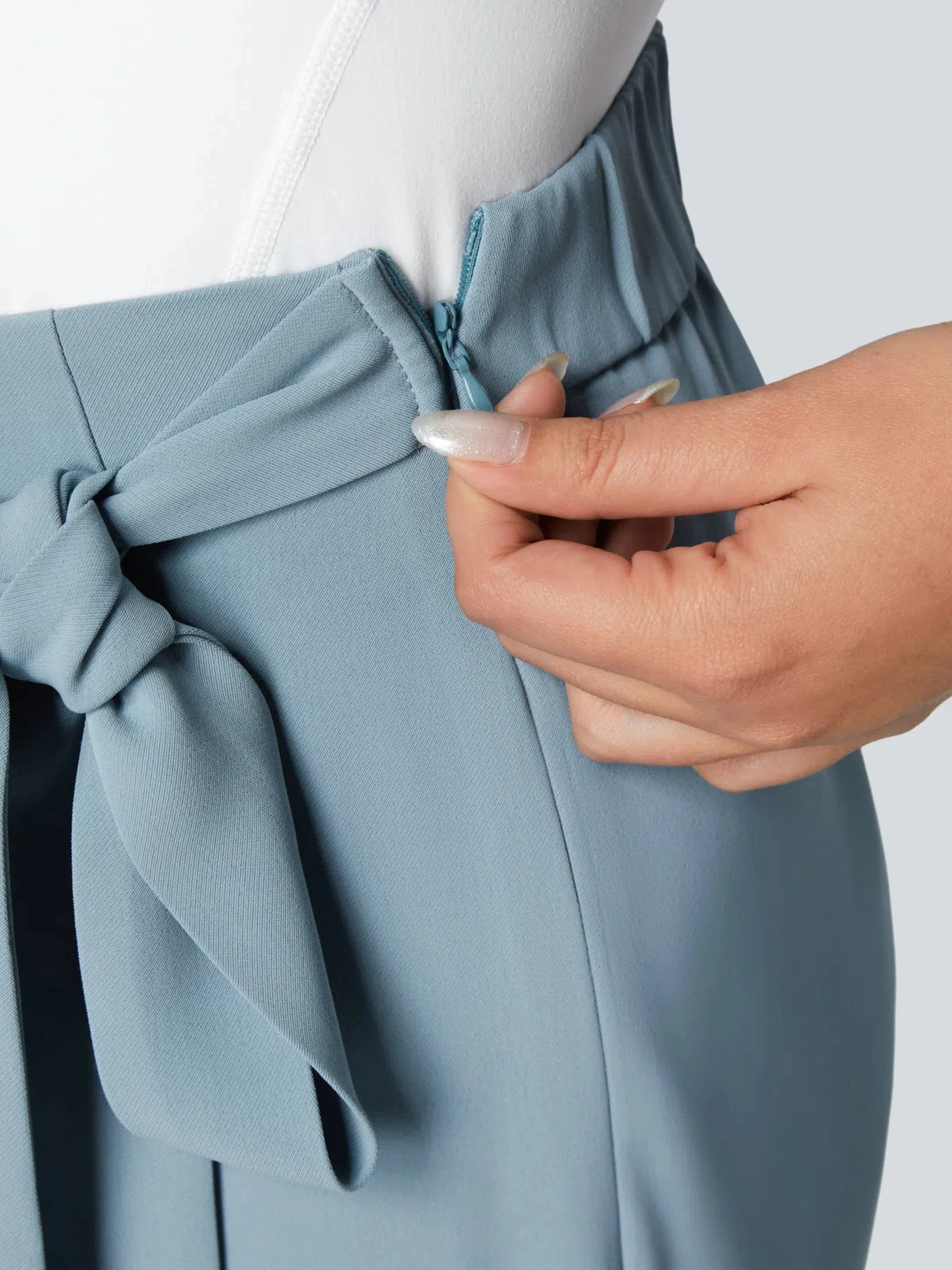 Person adjusting a blue garment on a mannequin with a white background