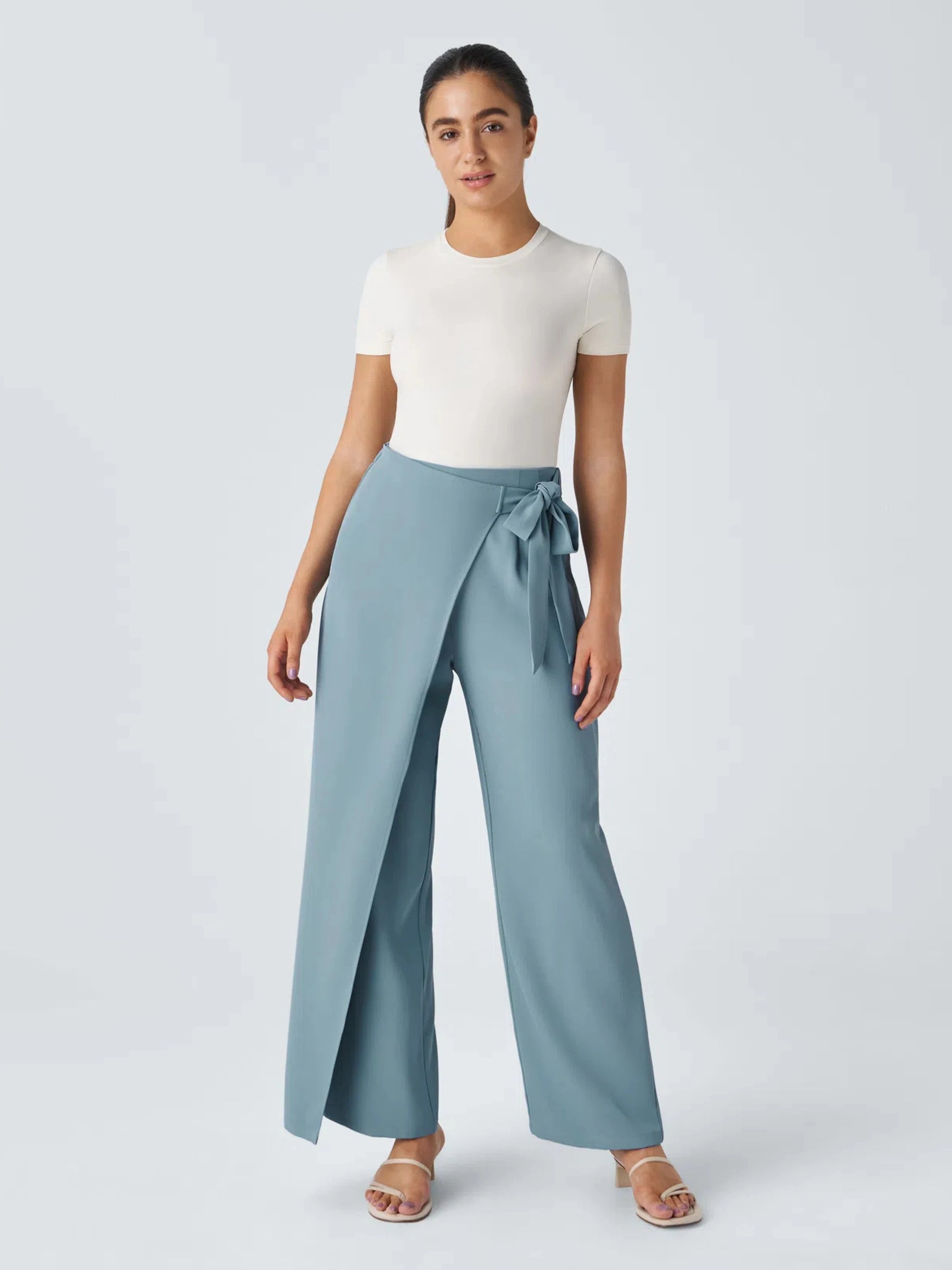 Woman wearing a white top and light blue wide-leg pants with a tie waist on a plain background